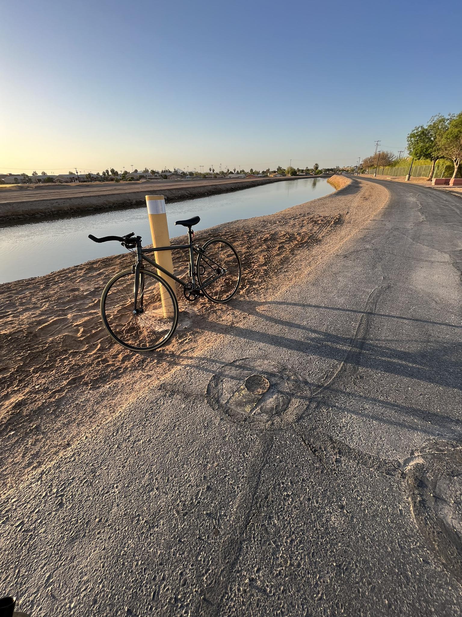 Bicycle parked on a paved path beside a canal at golden hour.