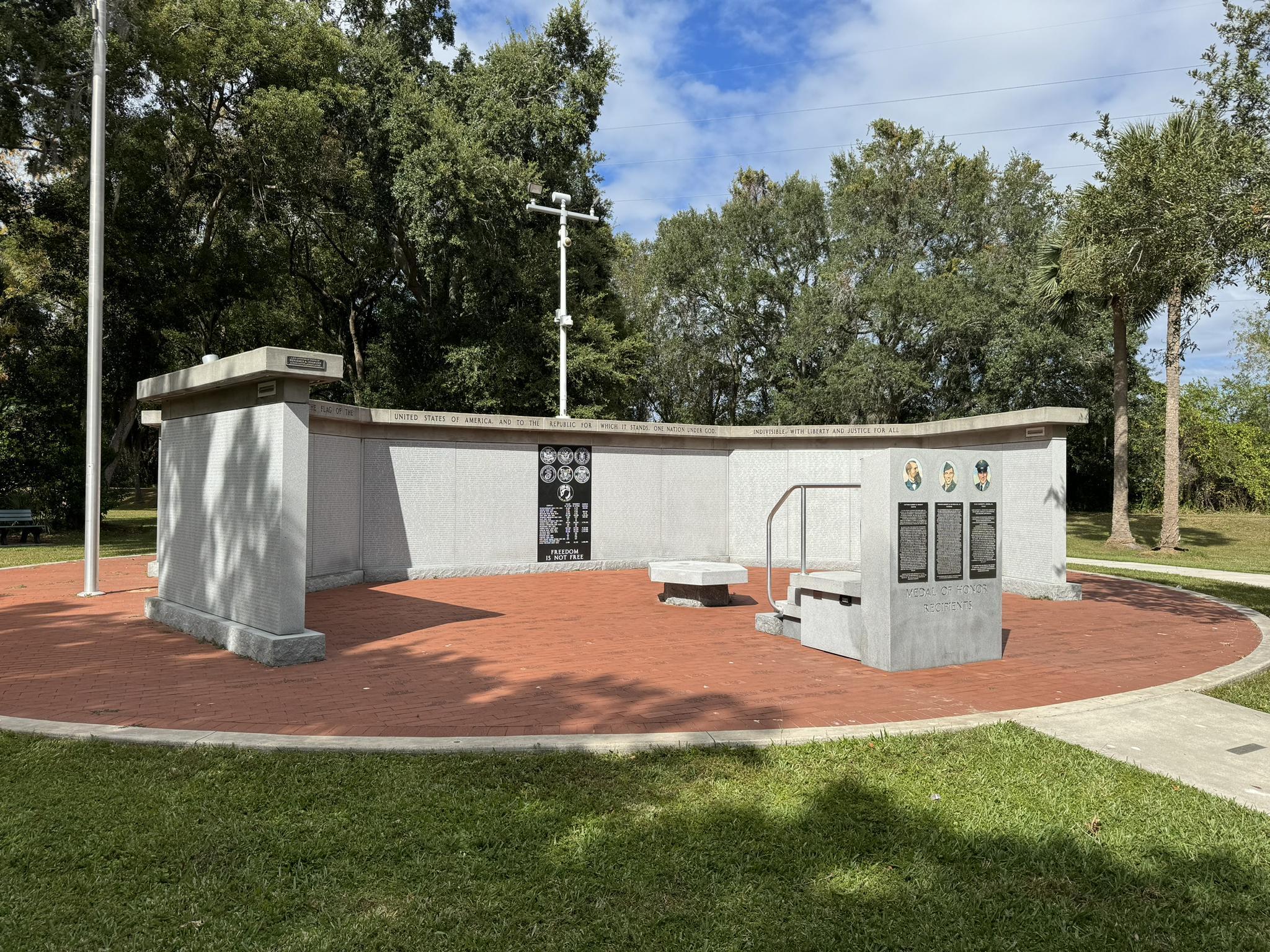 Concrete memorial with flagpole on a brick patio surrounded by green trees.