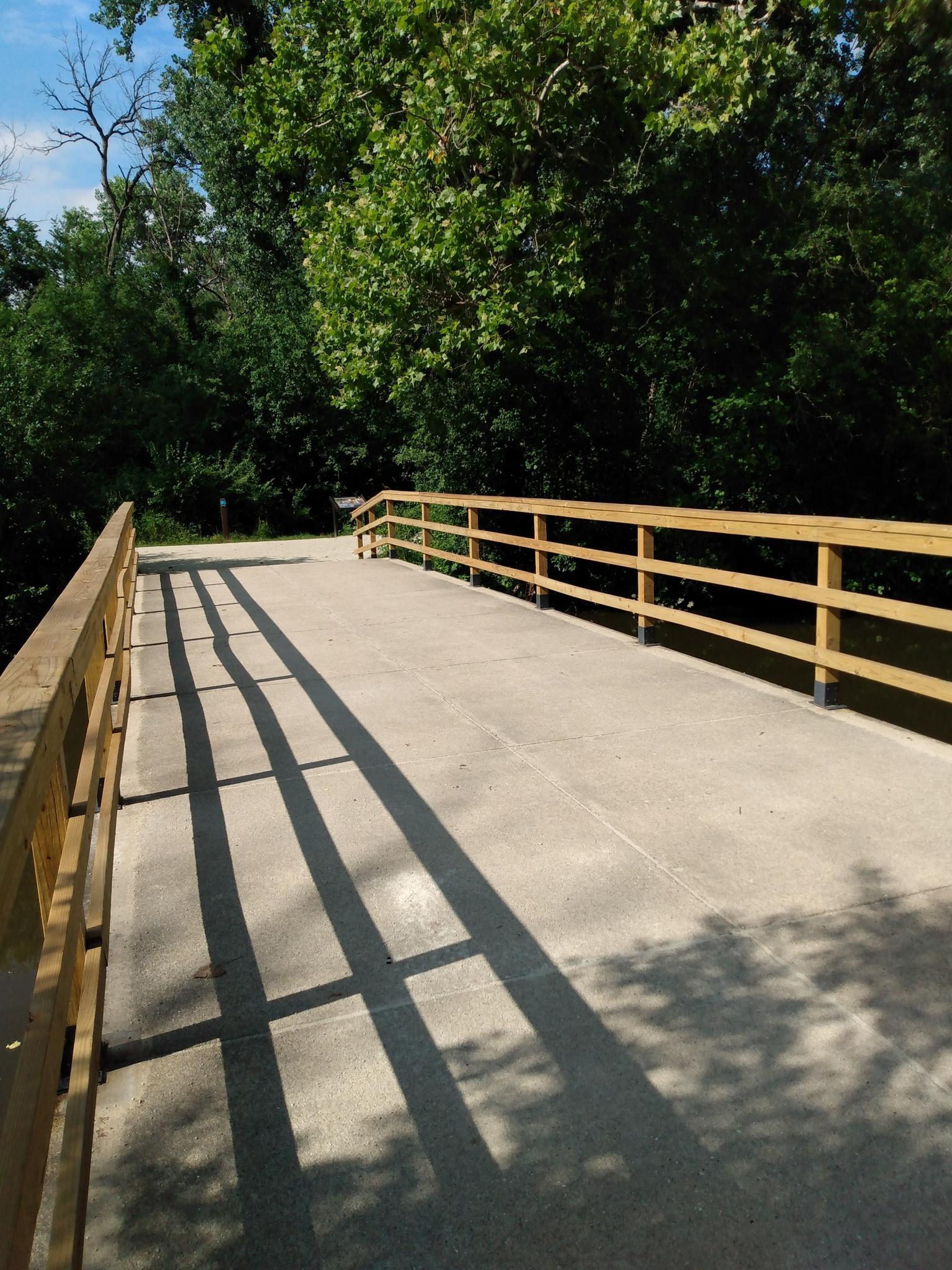 A concrete bridge with wooden railings casts long shadows on a sunny day.