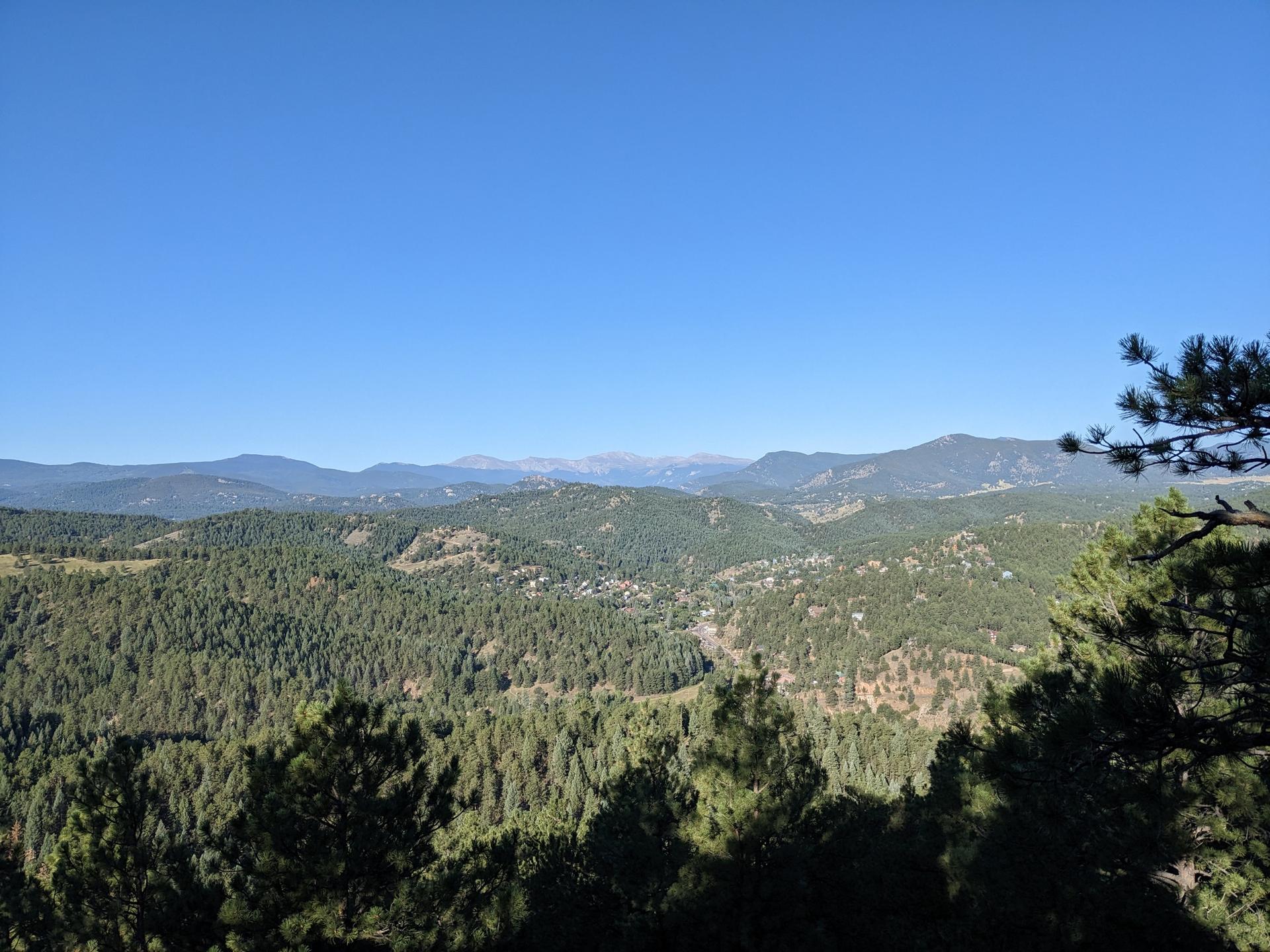 Expansive view of a vast forested mountain range under clear blue sky.