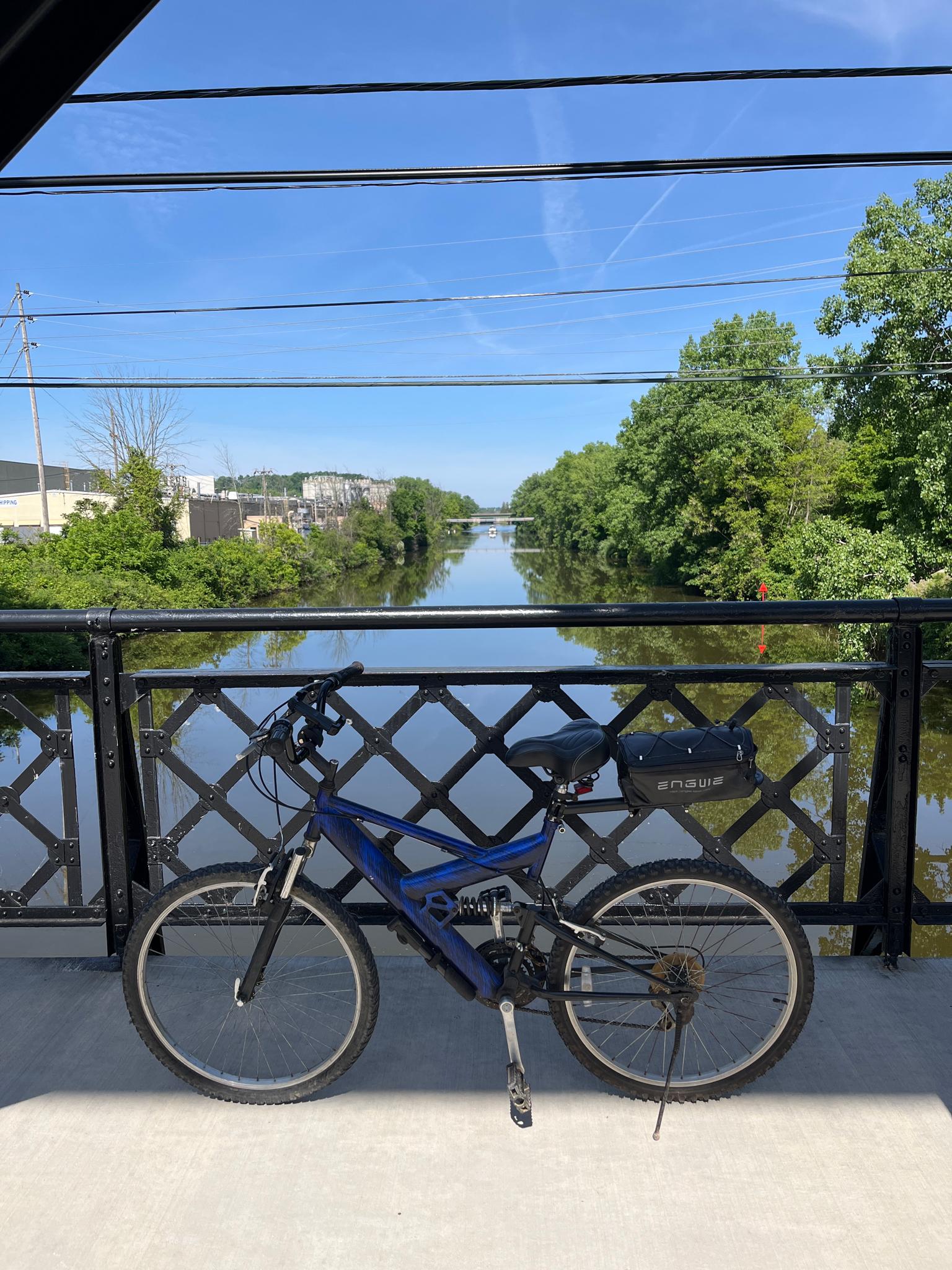 A blue bicycle rests on a bridge overlooking a river on a clear day.