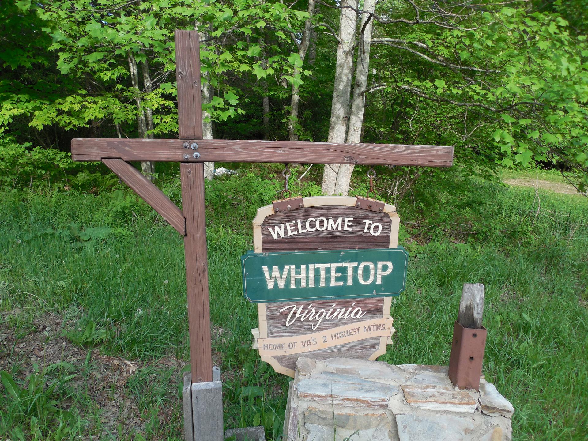 Wooden sign on a post, surrounded by green grass and trees.