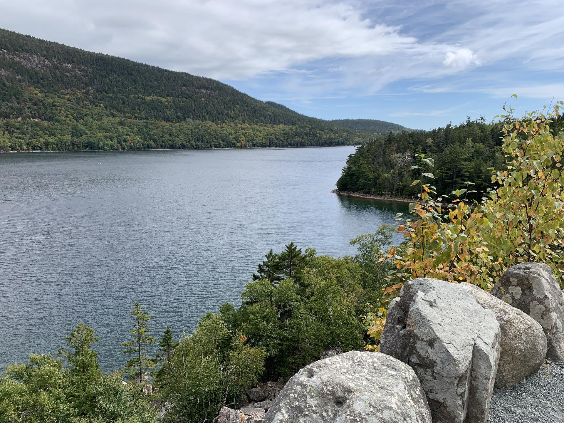 Wide lake view from a rocky overlook, forested hills, cloudy sky.