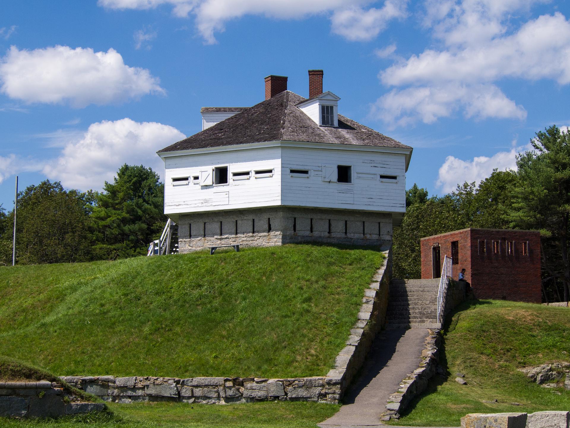 White octagonal building on a sunny grassy hill with a blue sky.
