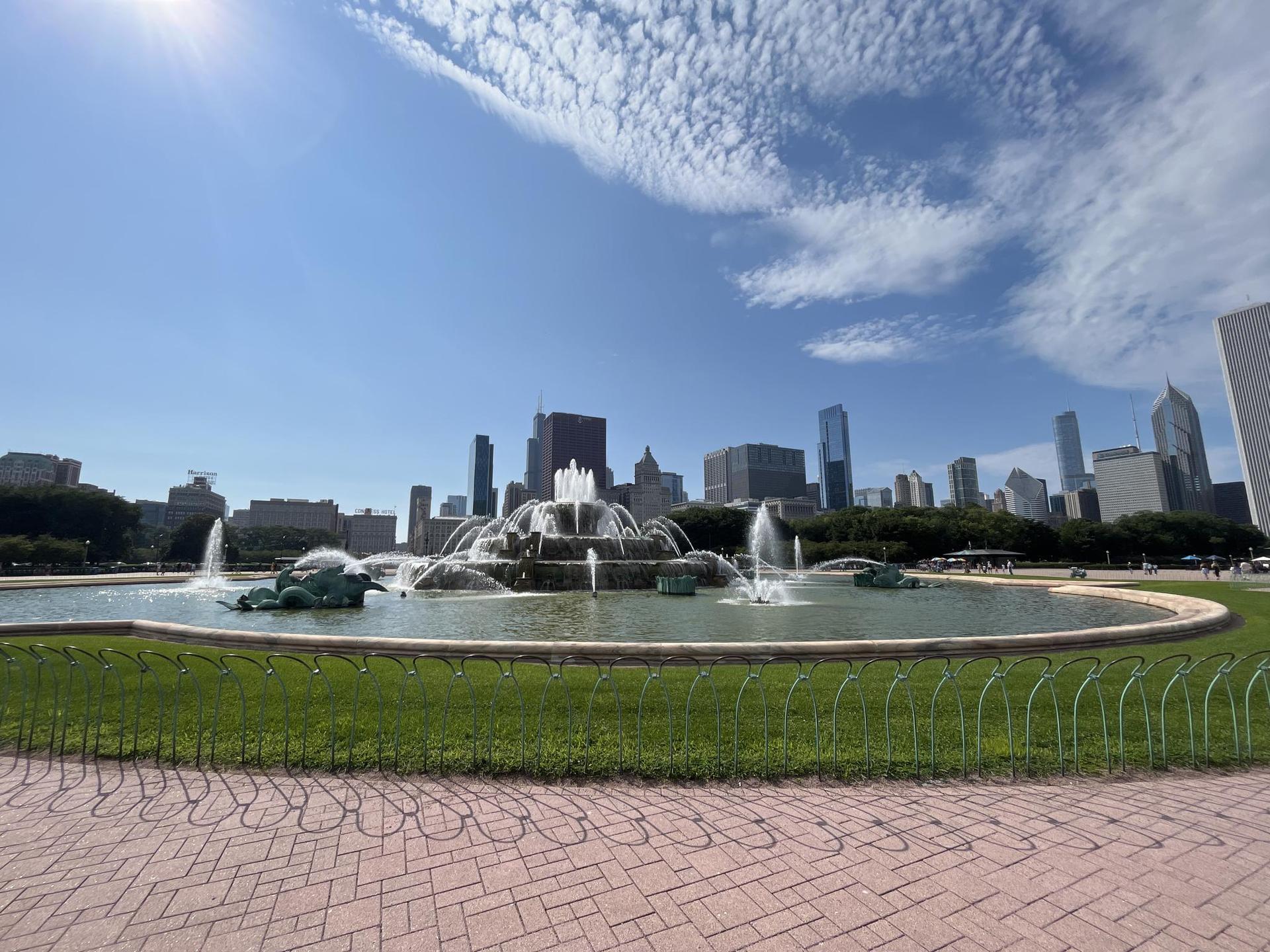 A large ornate fountain sprays water with a city skyline in the background.