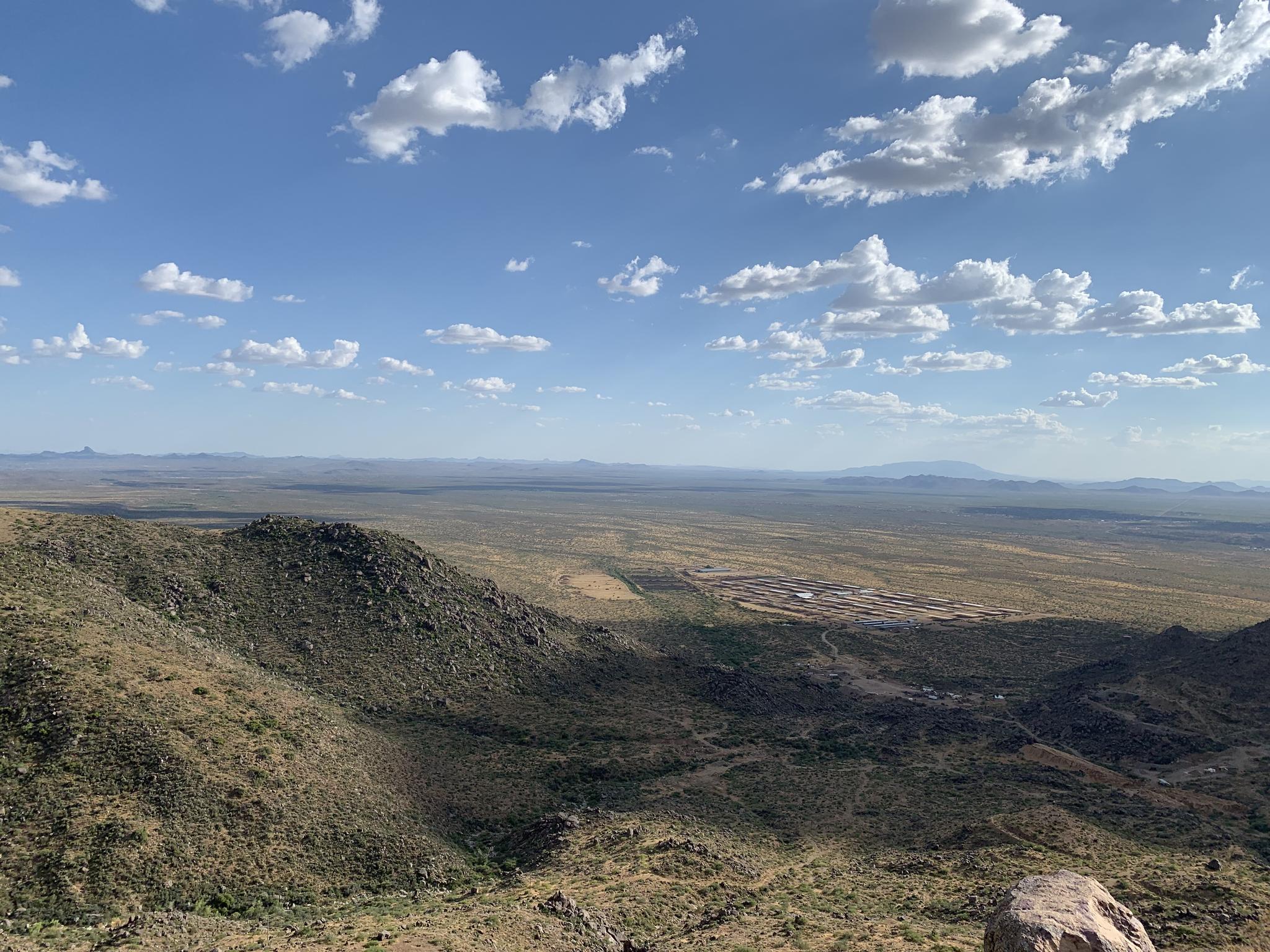 Expansive desert landscape with rocky hills, plains, and distant mountains under a bright sky.