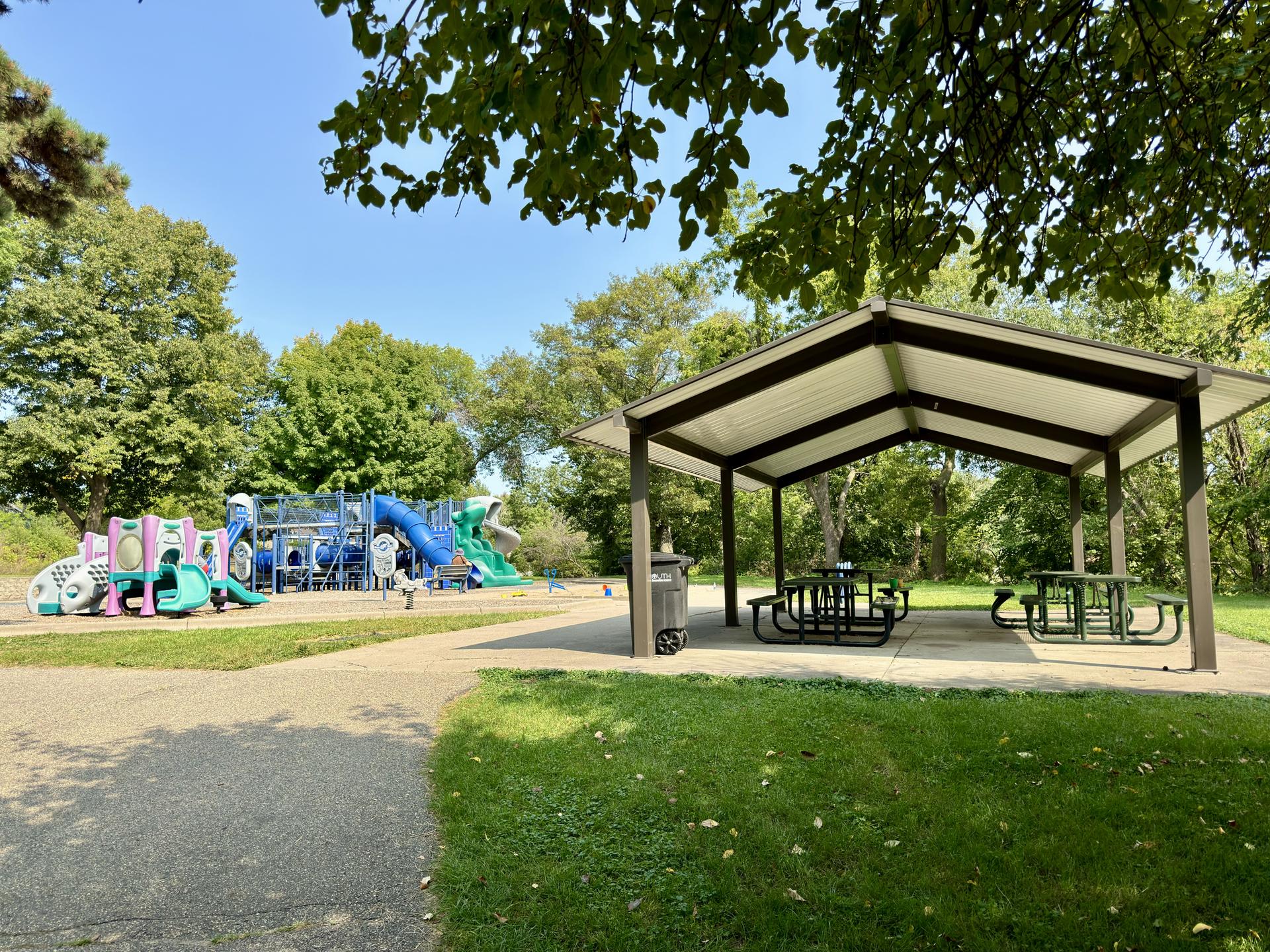 A colorful playground and picnic shelter in a sunny park.