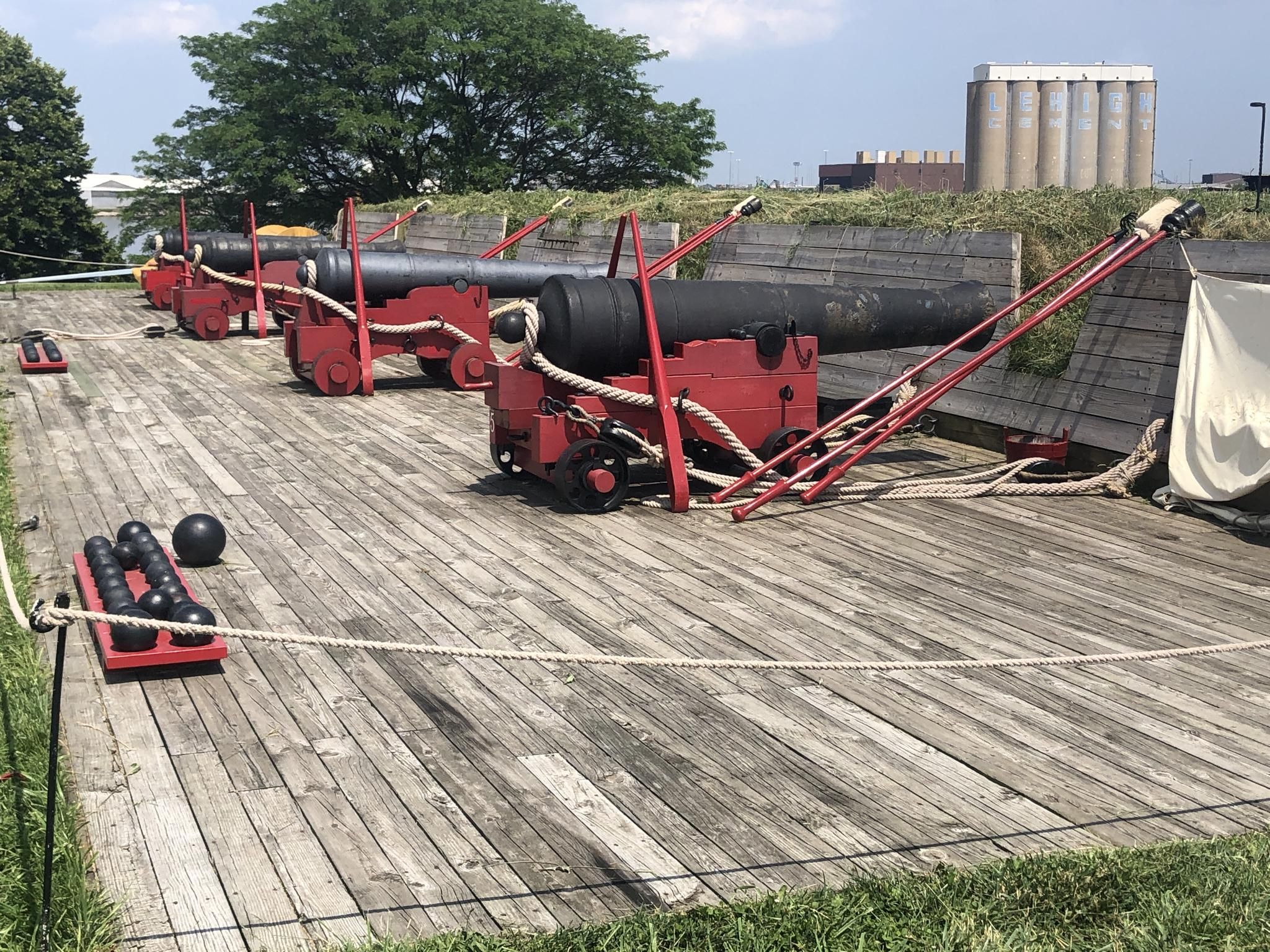 Historic cannons on red carriages lined up on a wooden deck in bright daylight. - Seawall Trail