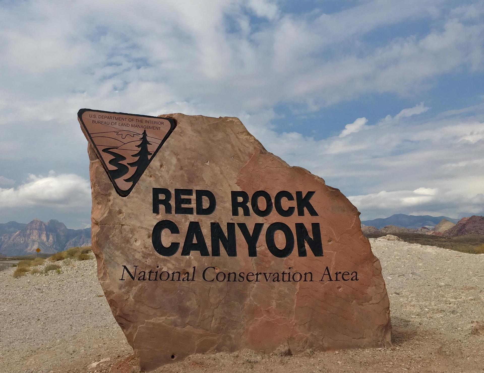A large rock sign with black text under a cloudy sky.