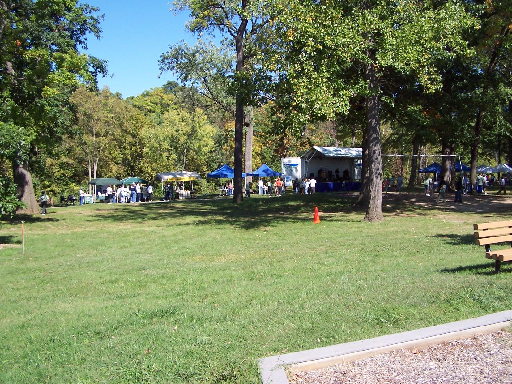 Sunny park gathering with many people, tents, and trees.