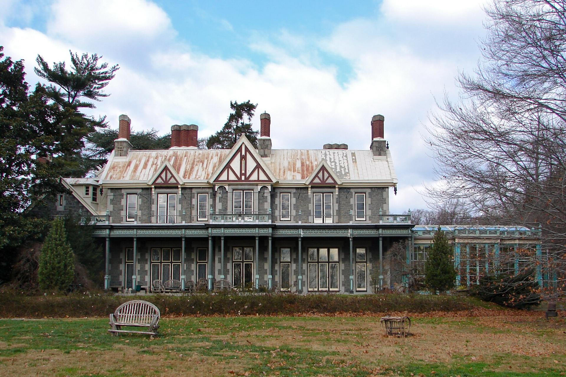 Large, weathered stone mansion with a green lawn under a cloudy sky.