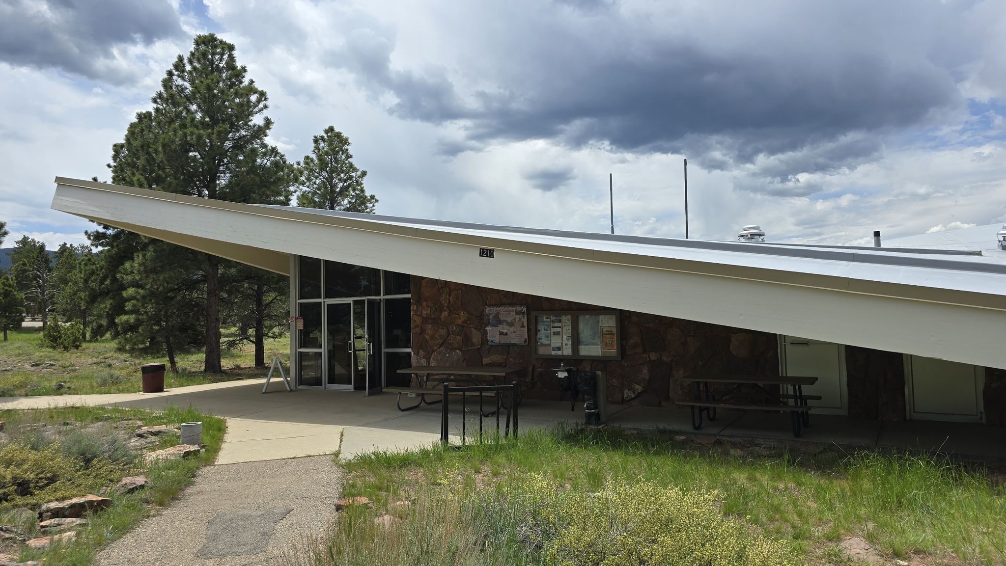 A modern building with a slanted roof and stone facade under cloudy skies. - Red Canyon Rim Trail