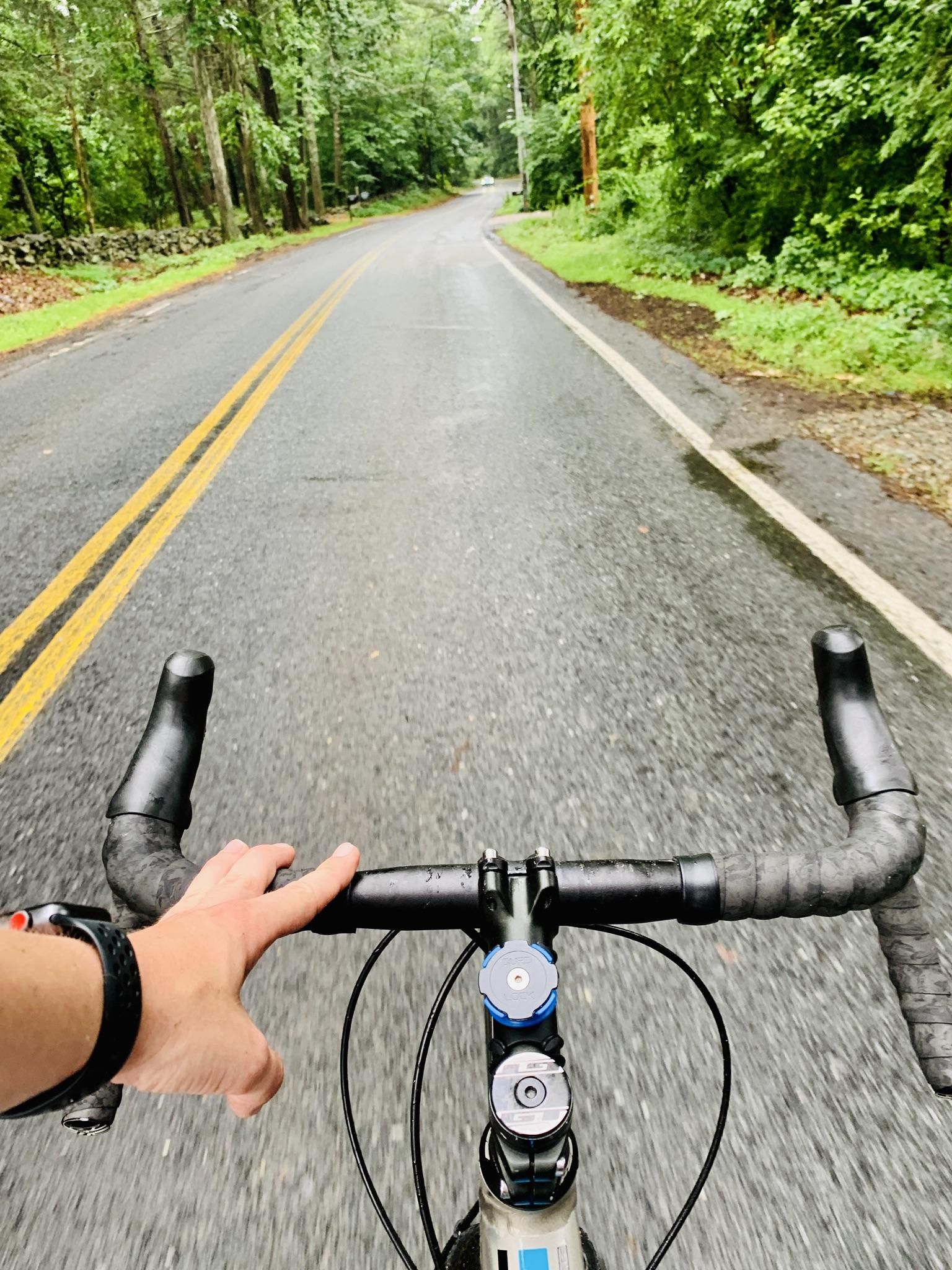 A person's hand on bicycle handlebars rides down a paved road. - Hale Reservation to Bussey Hill loop via Charles River Conservation Land