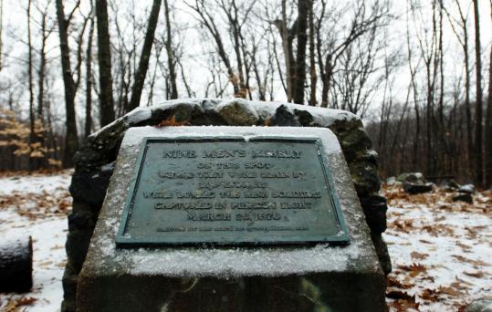 A snow-dusted historical marker in a bare winter forest on an overcast day.