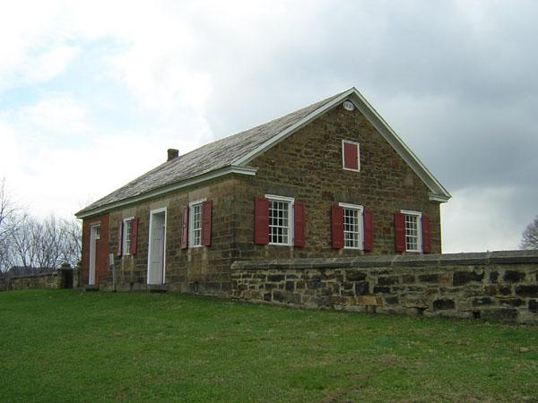 Old stone building with red shutters and a stone wall under an overcast sky.