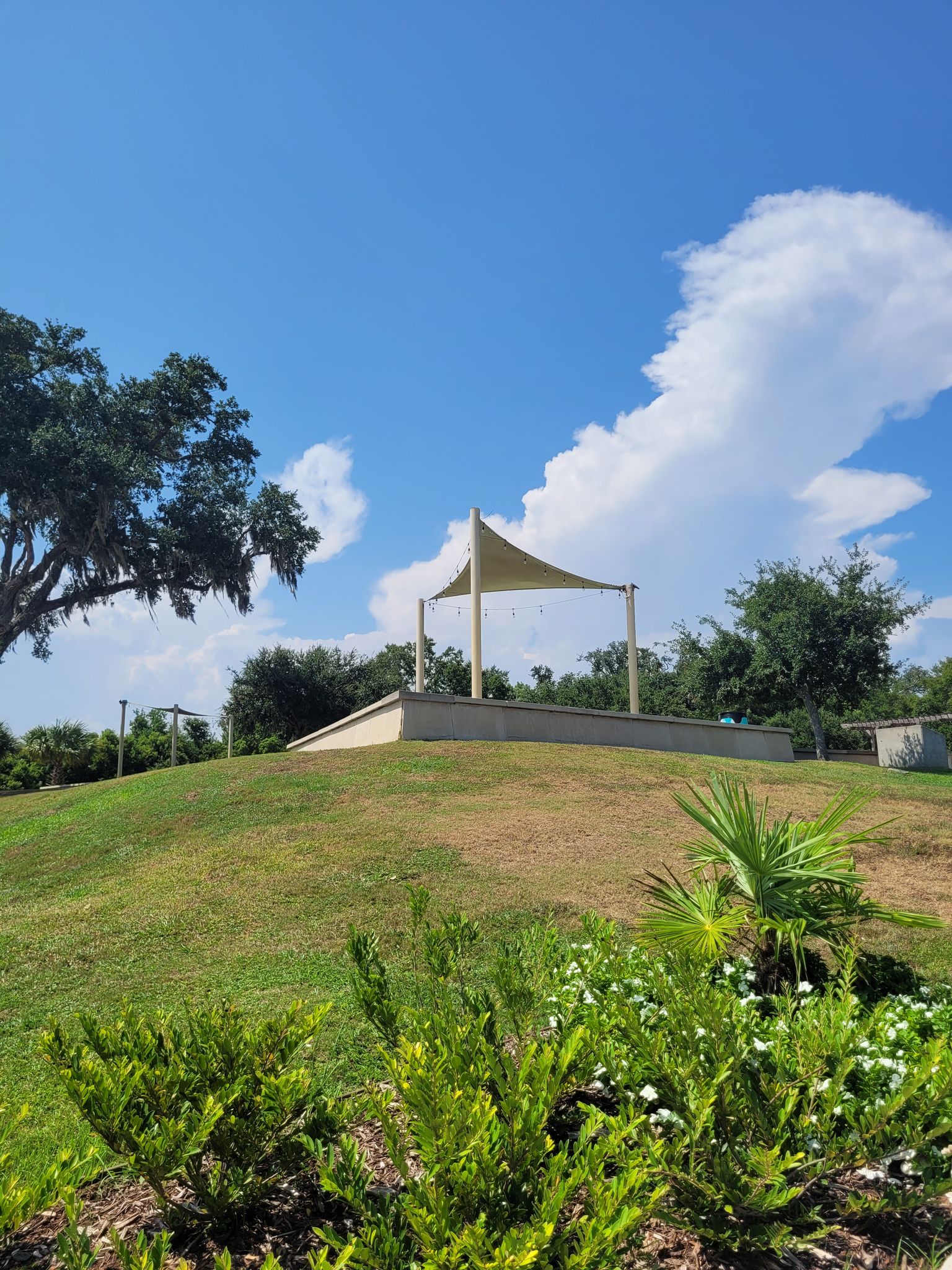 Outdoor stage with a fabric canopy on a grassy hill under a bright blue sky. - Front Beach Walking Path