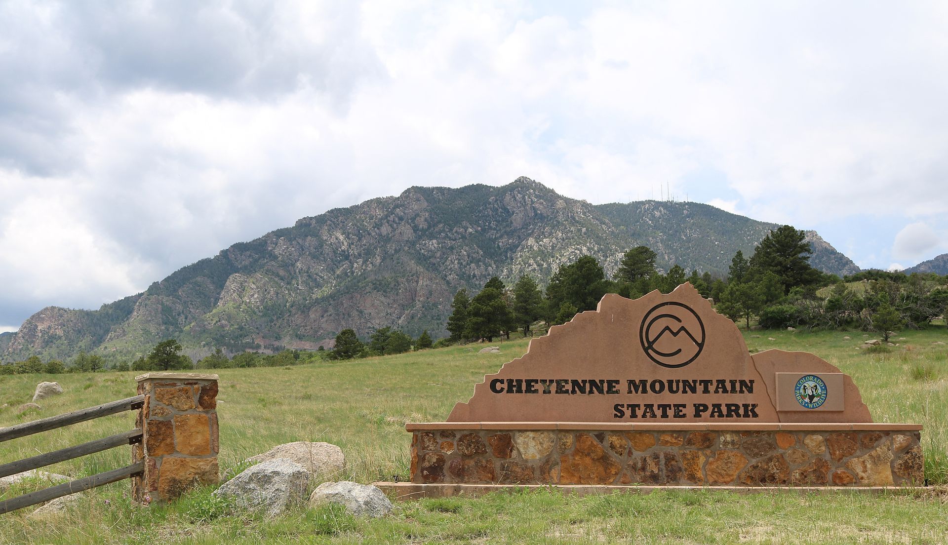 A large park sign in a grassy field with a mountain under a cloudy sky. - Cheyenne Mountain via Talon and Dixon Trail