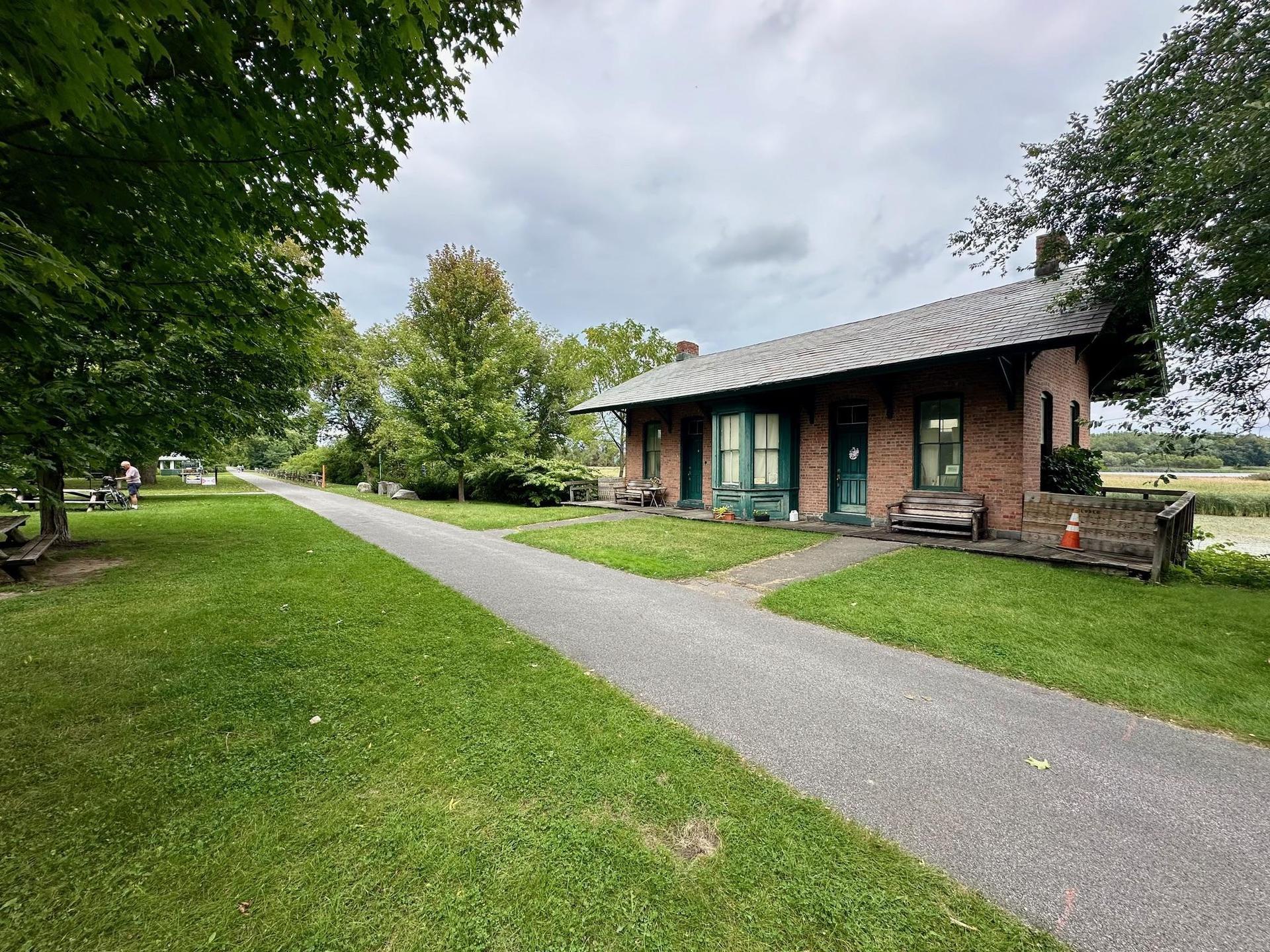 Brick building with green trim next to a paved path on a cloudy day.