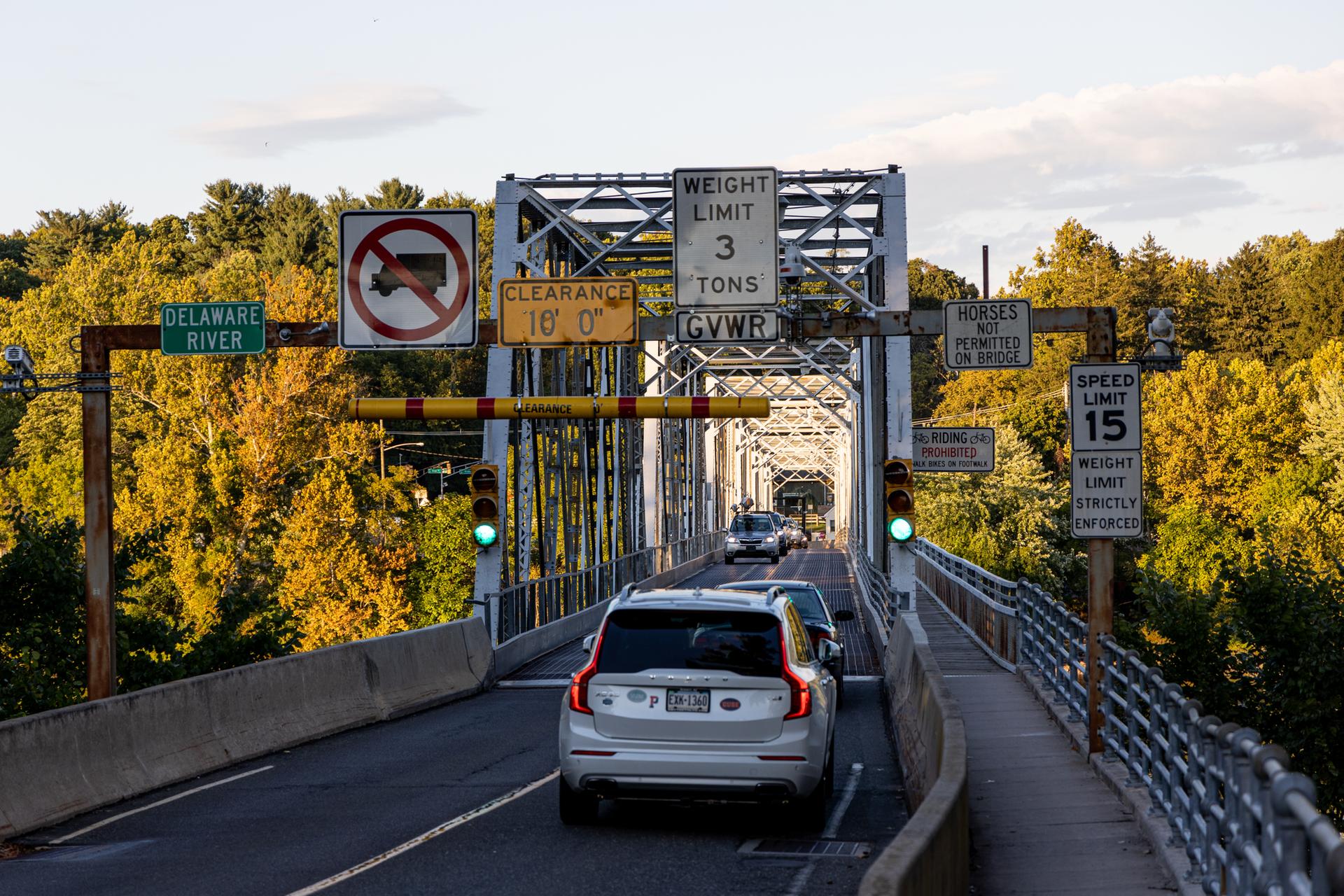A white SUV drives onto a metal truss bridge at golden hour.