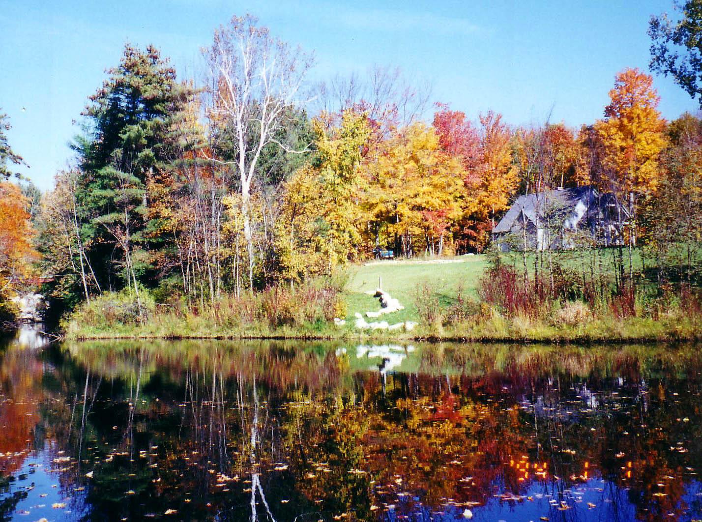 Vibrant autumn trees and a house reflected in a calm lake on a bright day.