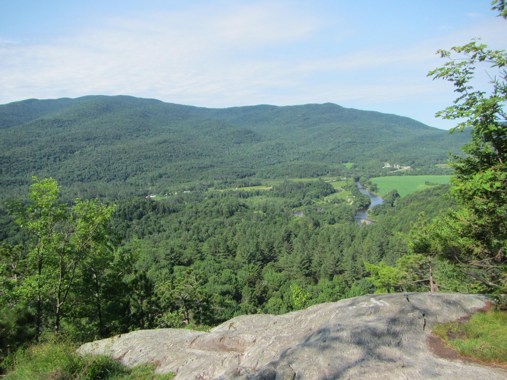 Overlooking a lush green valley, river, and forested mountains on a clear day.