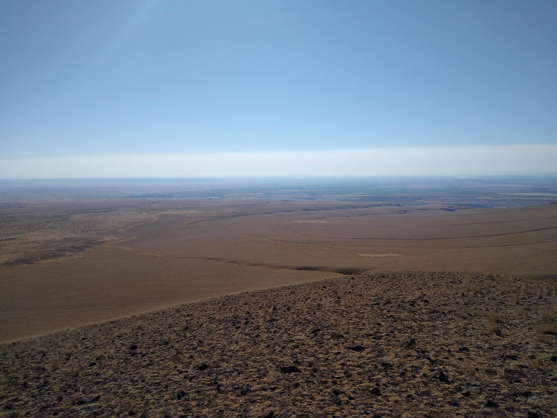 Expansive arid plains stretch under a clear blue sky on a bright day.