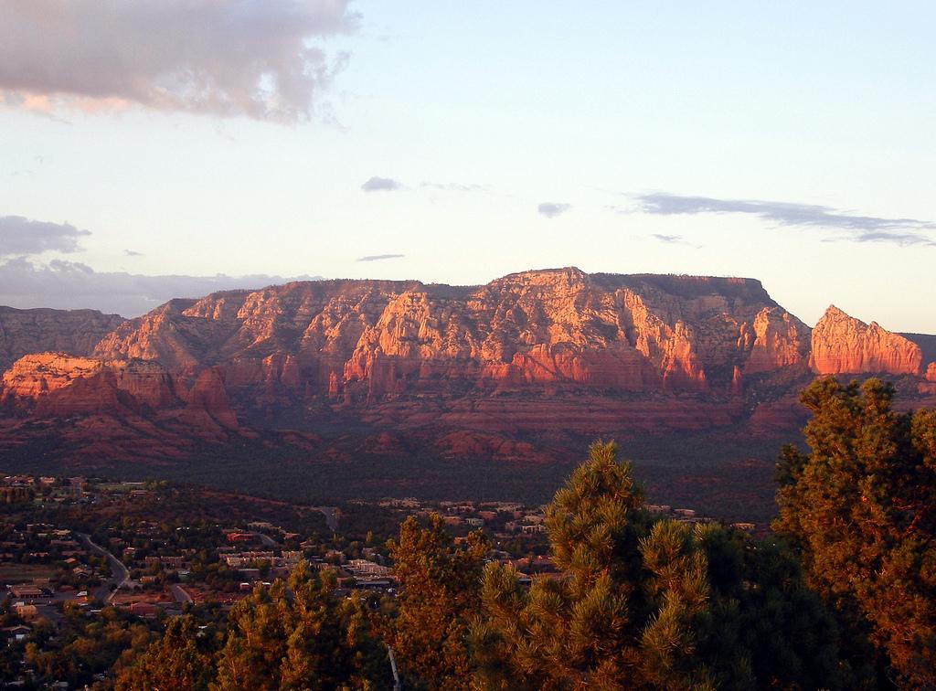 Golden hour light illuminates red rock mountains above a sprawling town.