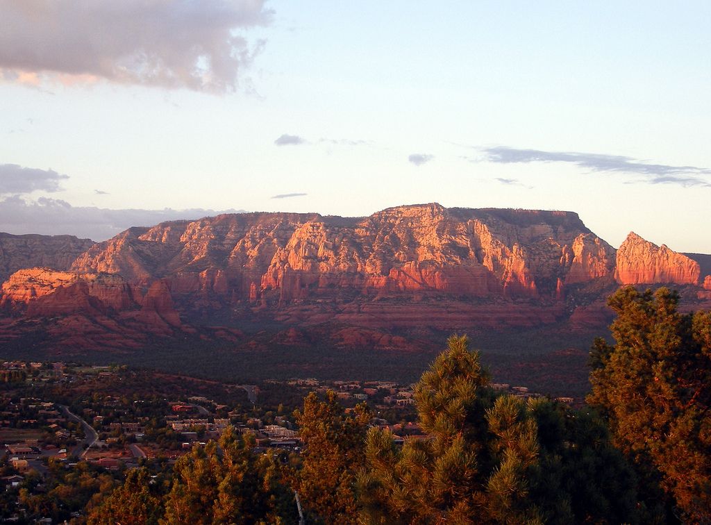 Golden hour light illuminates red rock mountains above a sprawling town. - Thunder Mountain Road Bike Route