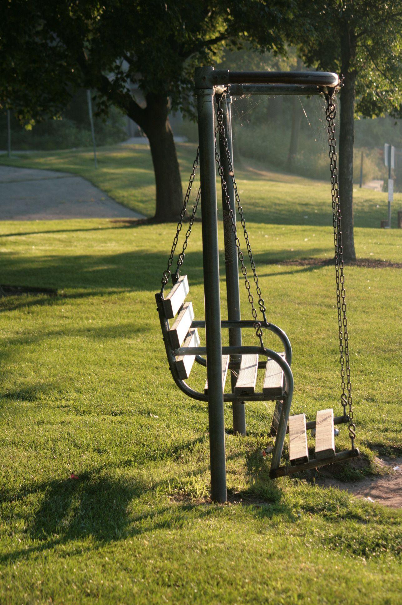 Empty swing set in a sunny park with long shadows from trees.