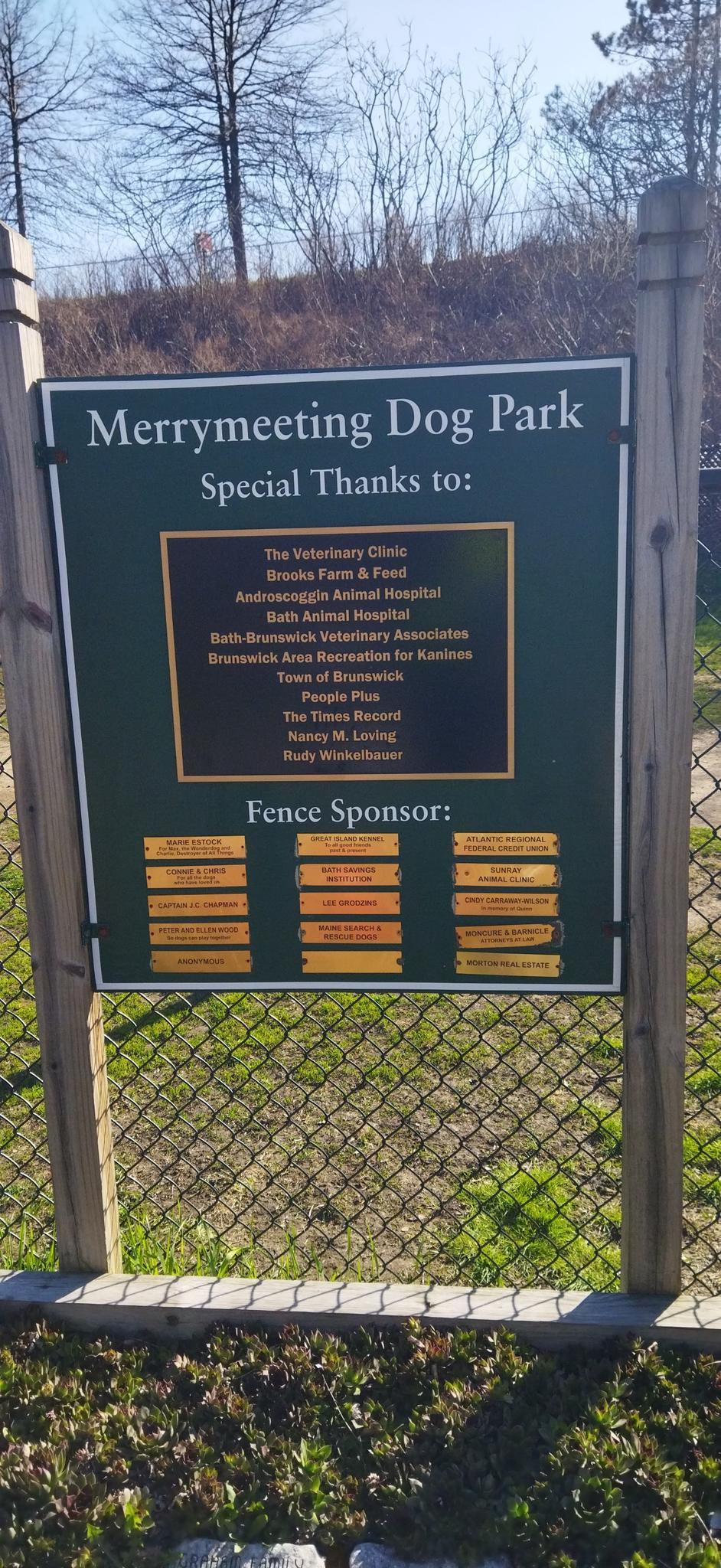 A dog park sign with sponsor names stands in bright sunlight.