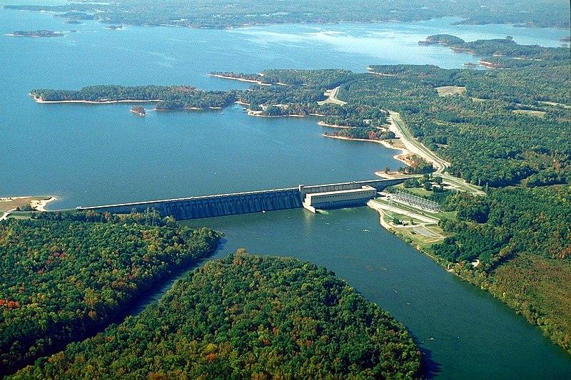 Aerial view of a large dam spanning a wide river surrounded by green forests.