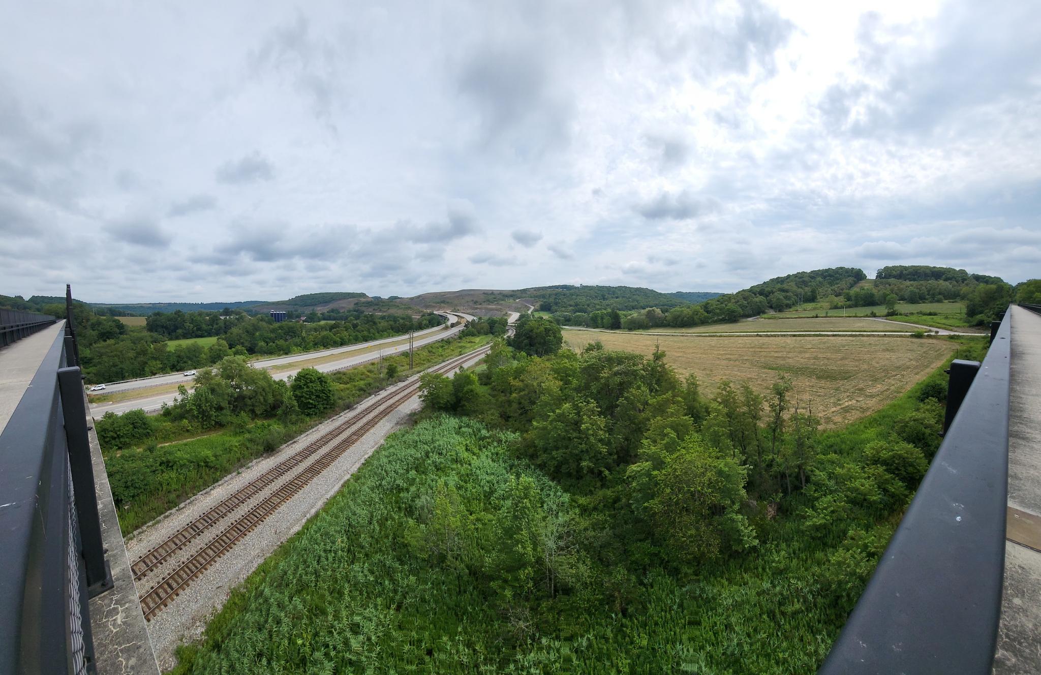 An overcast view of parallel train tracks and a highway through green landscape.