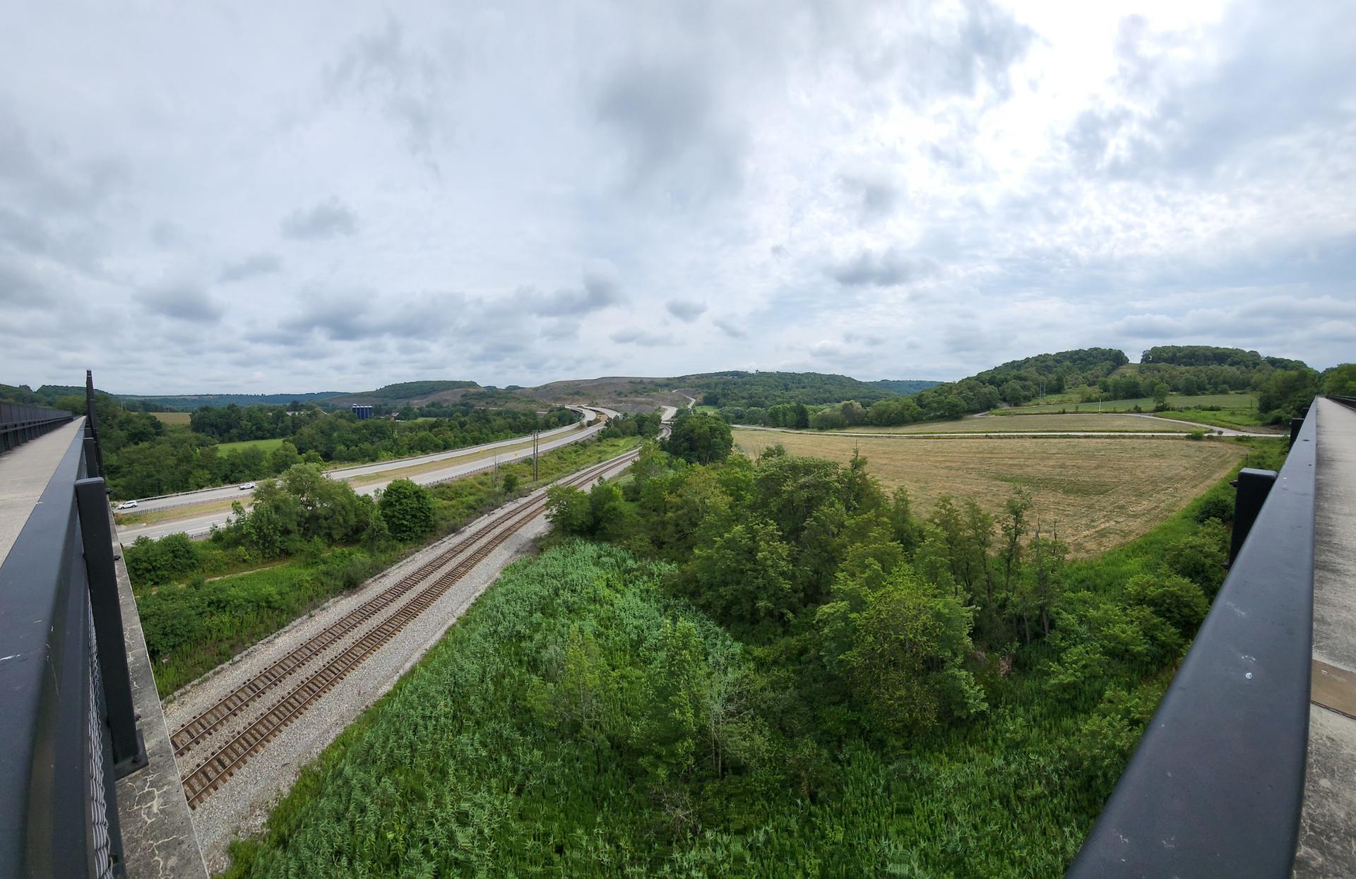 An overcast view of parallel train tracks and a highway through green landscape.