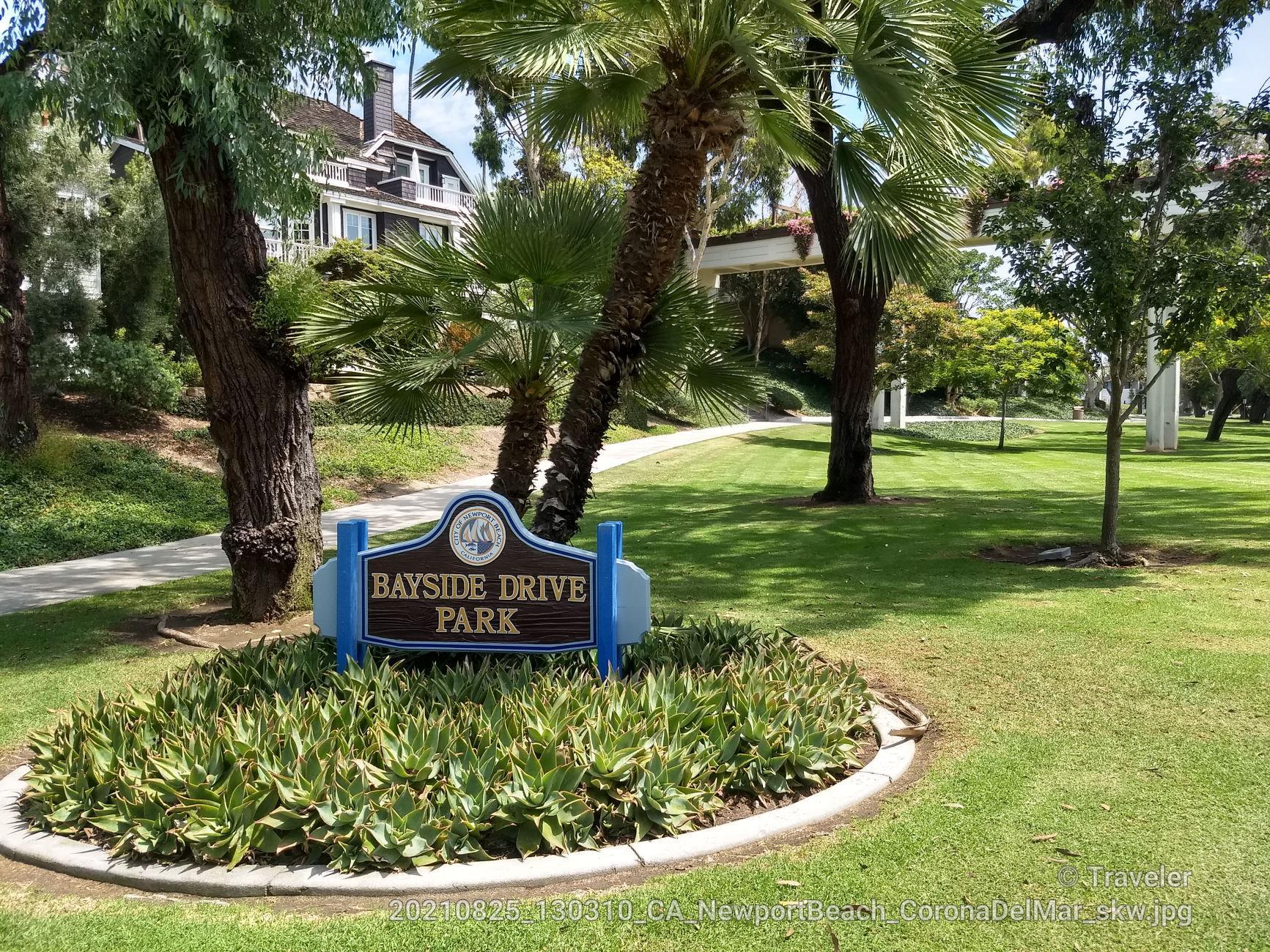 Park sign surrounded by green grass and palm trees on a sunny day.