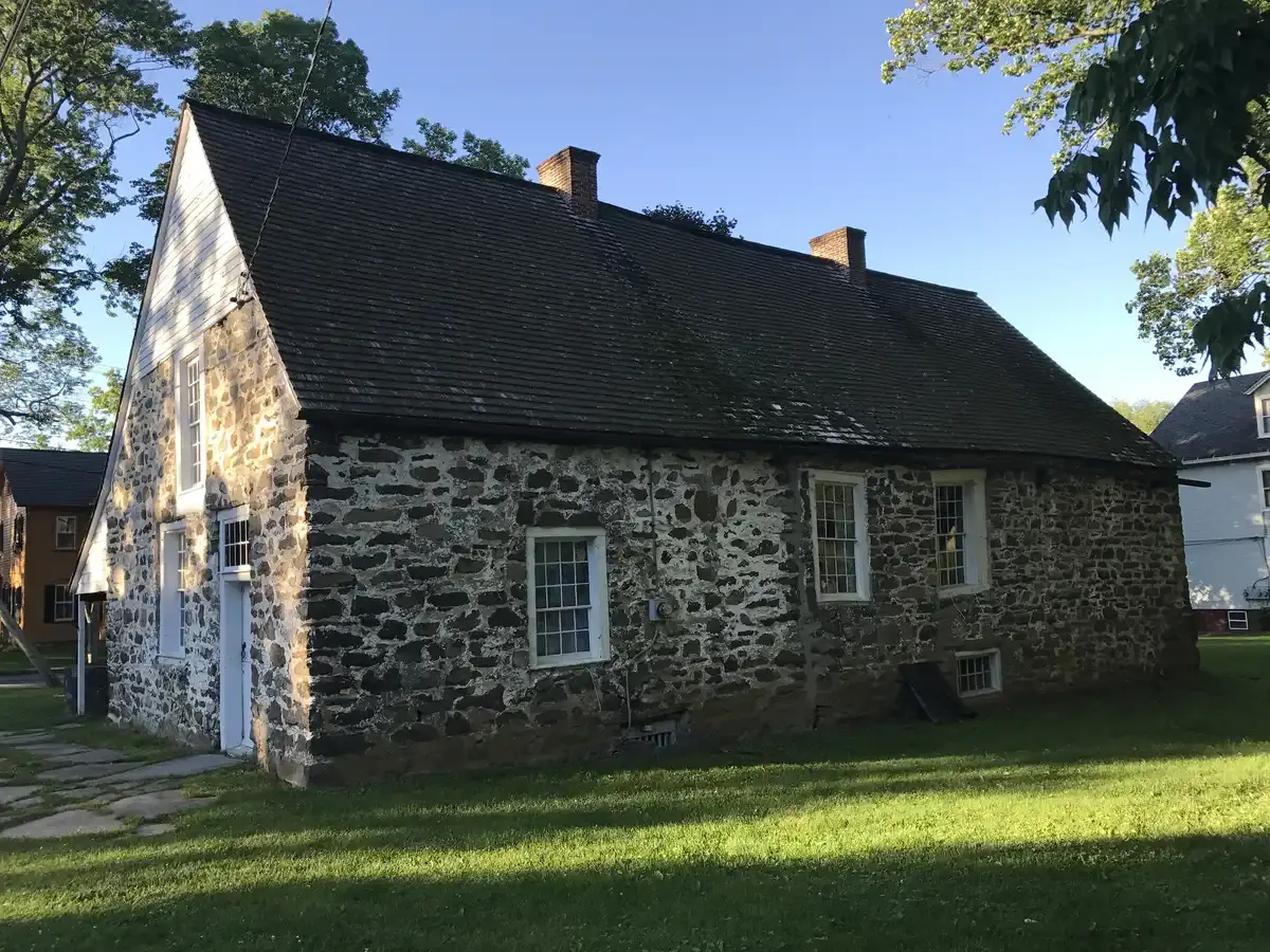 Sunny view of an old stone building with a dark roof and green lawn.