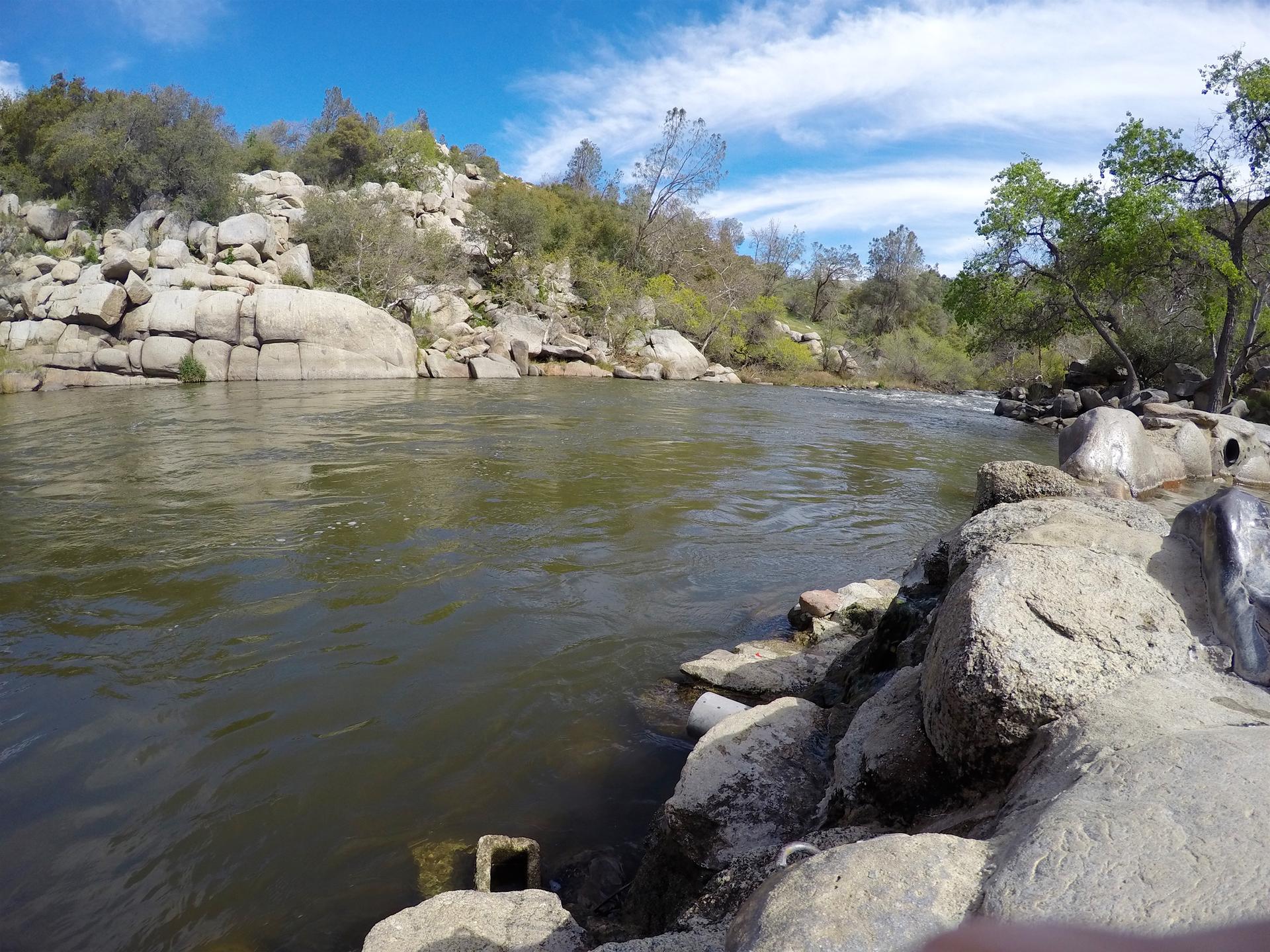 A wide river flowing past large rocks and green, rocky banks.