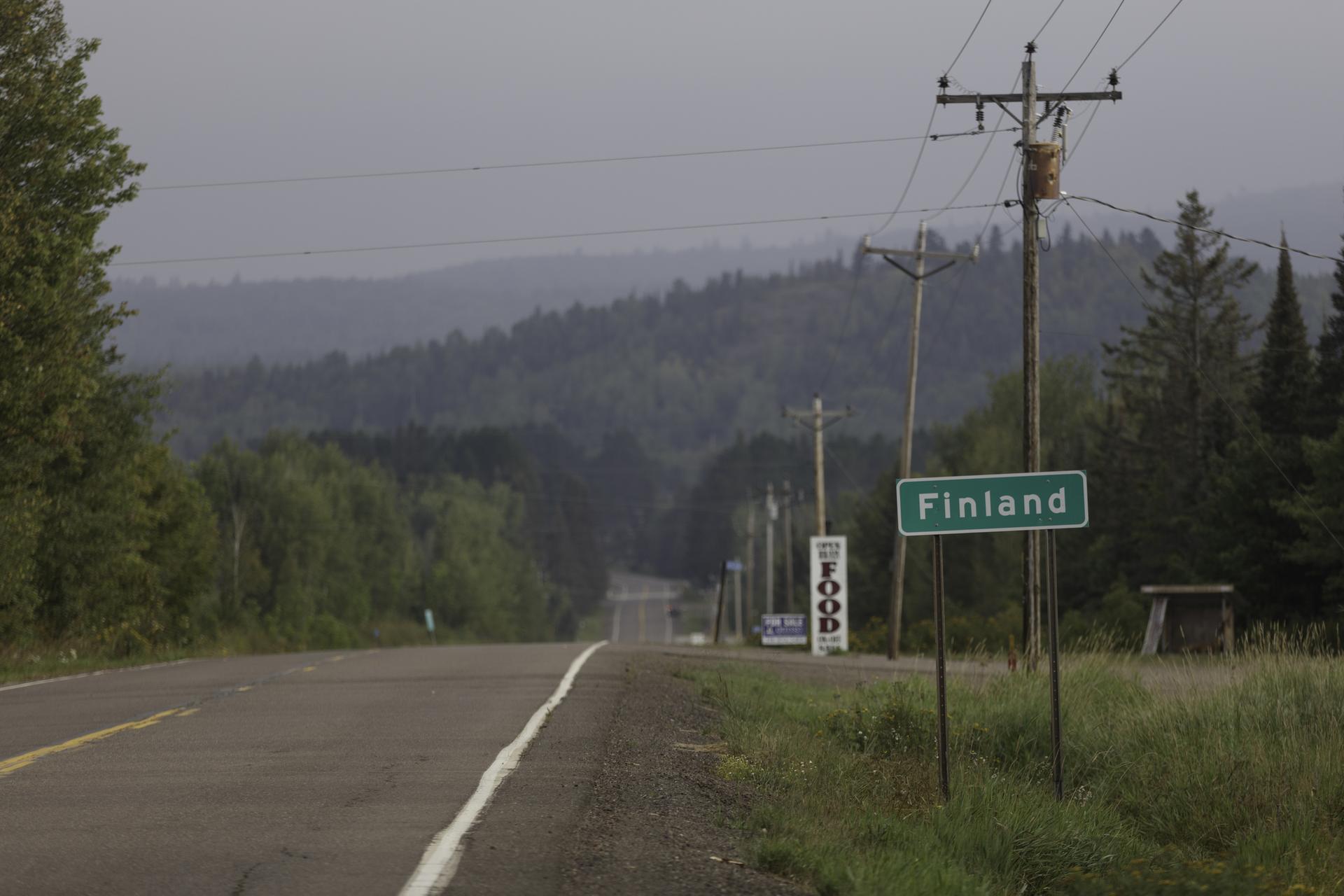 Rural road leading into forested hills under an overcast sky.