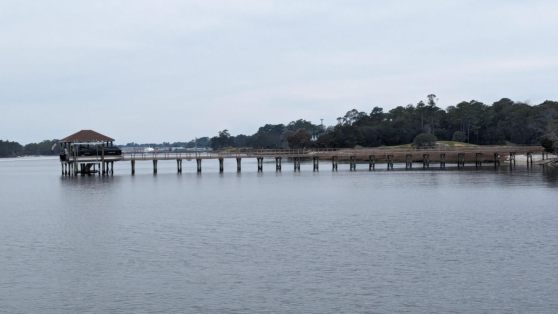Long wooden pier with a covered structure extending over calm water, overcast.