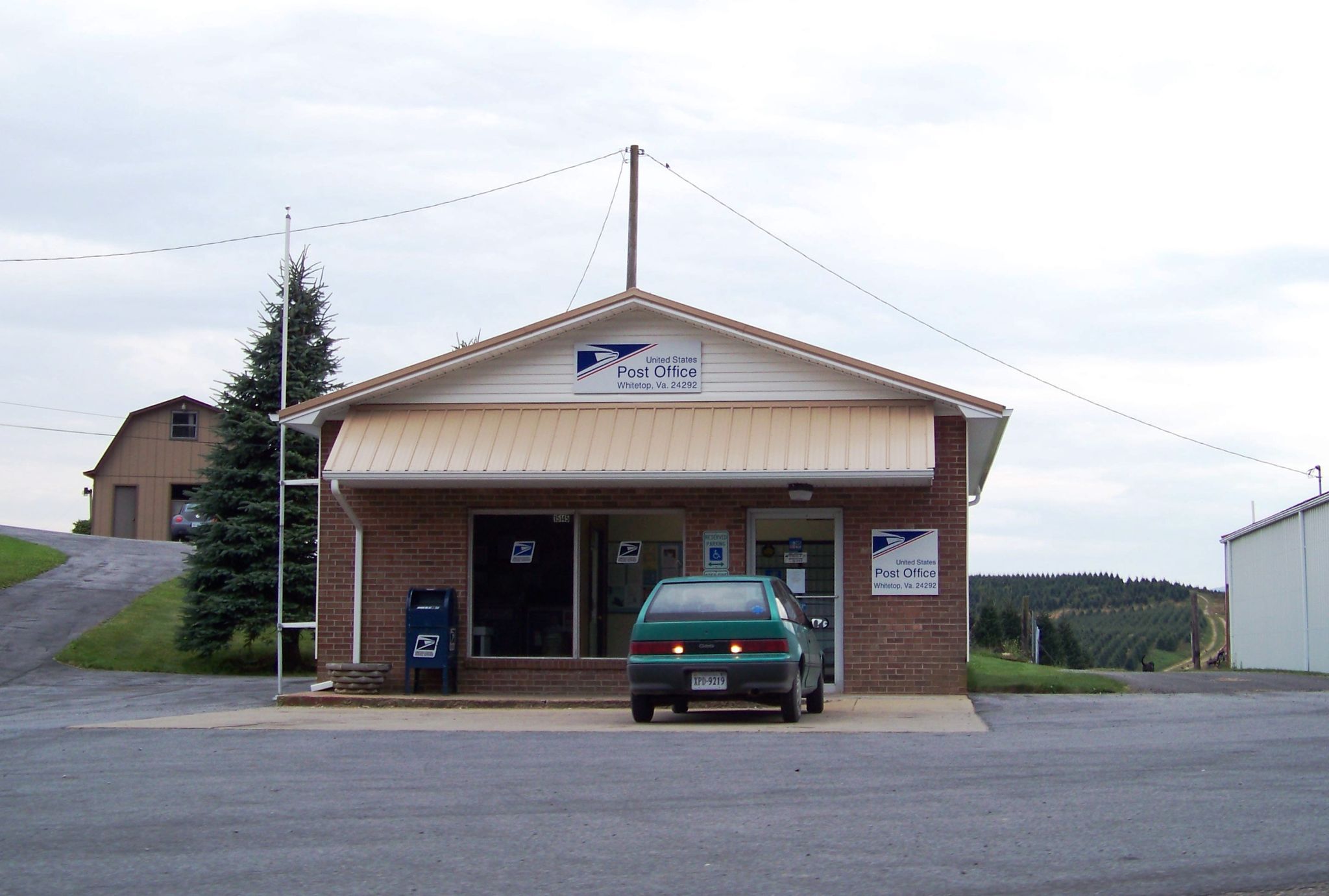 Small brick building with a green car parked in front under a cloudy sky. - Whitetop Mountain loop