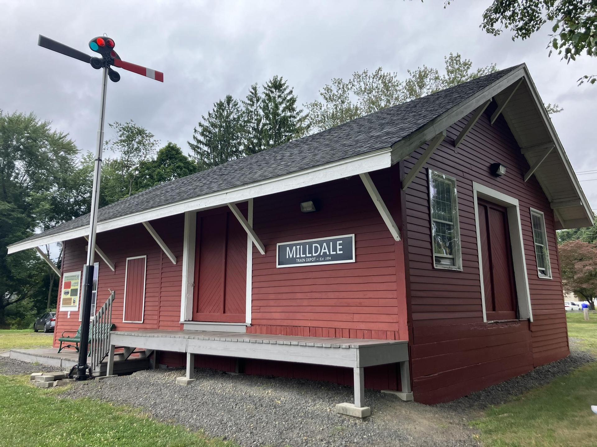 A small red wooden building with a sign and signal pole, under cloudy skies.