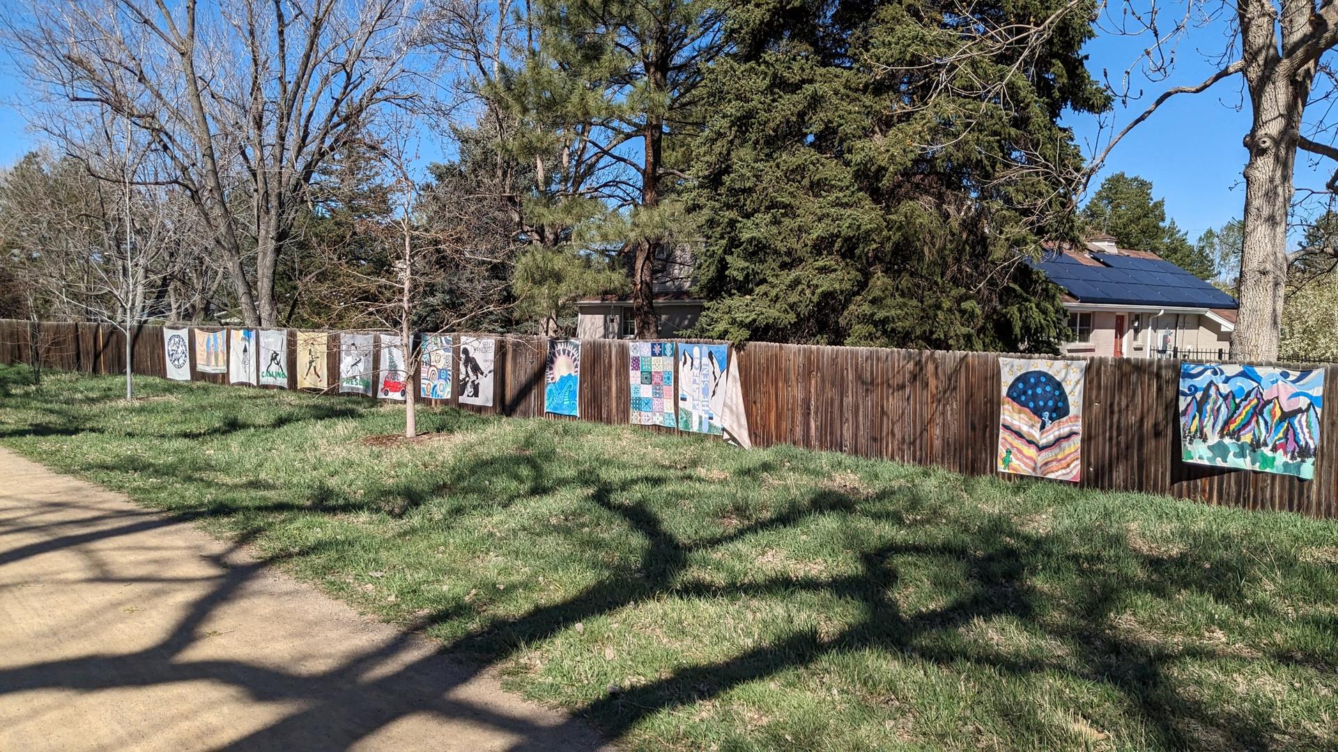 A long wooden fence adorned with colorful art panels under bright daylight.