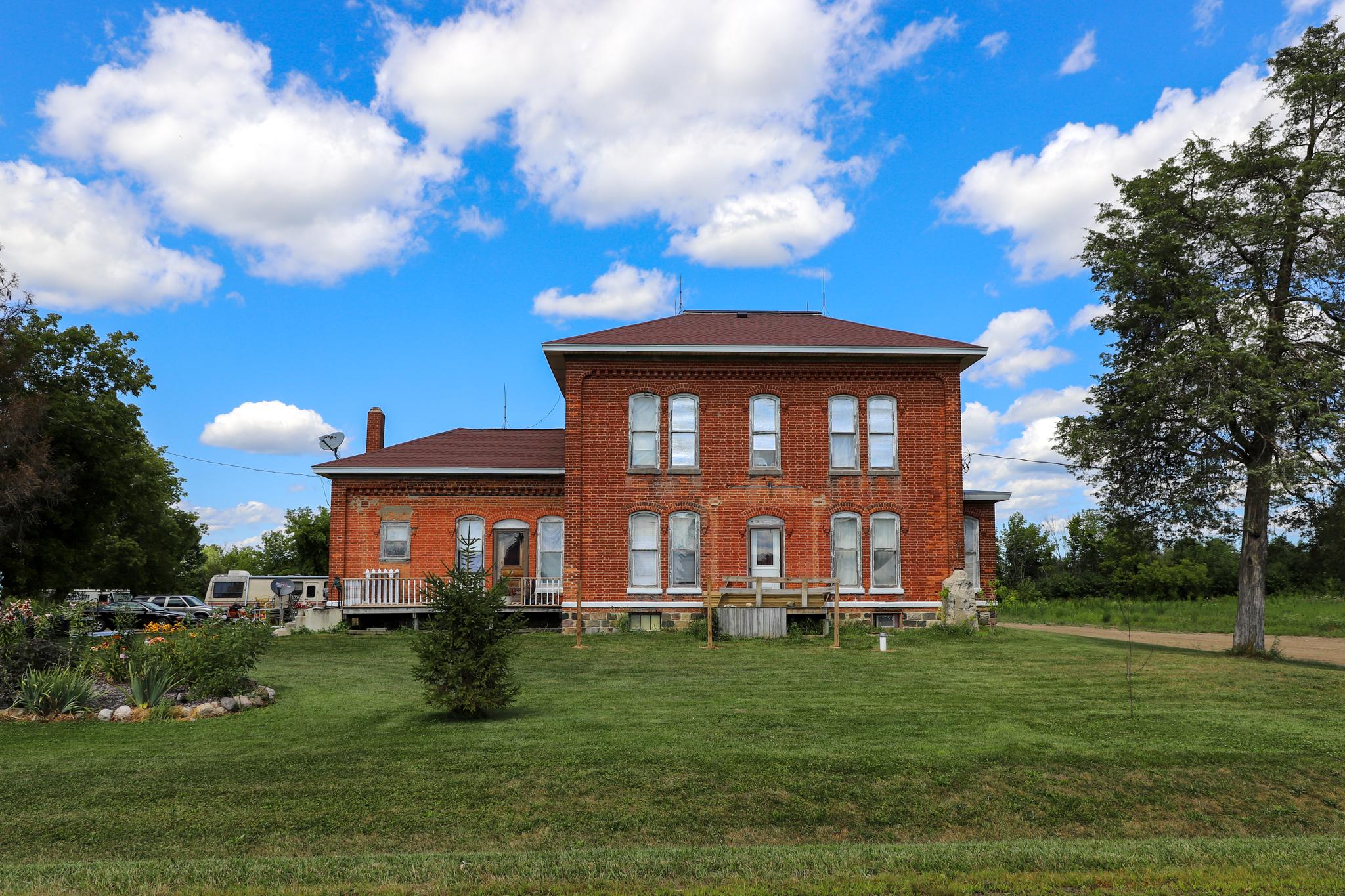 Large brick house with green lawn under a bright blue sky with clouds.