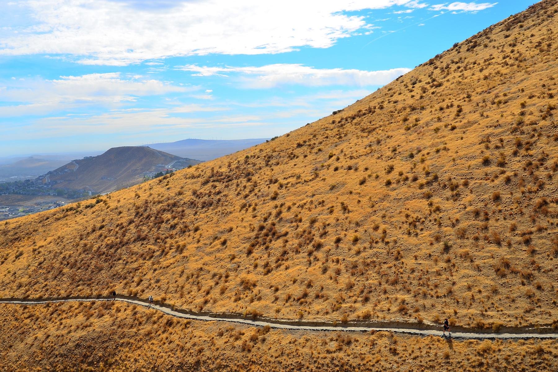A winding road traverses a golden, dry hillside under a bright sky.