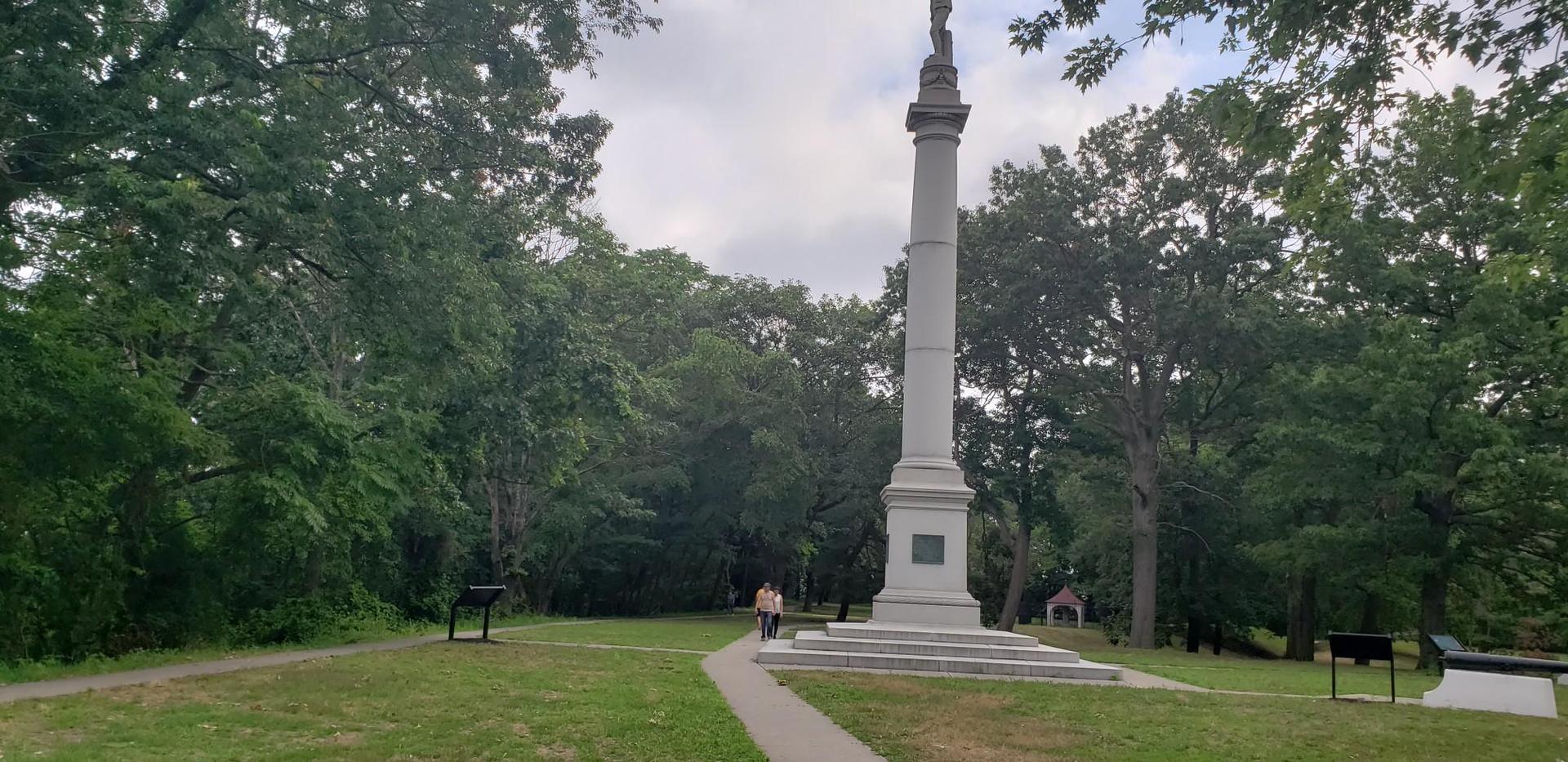 Person walks towards a tall stone monument in a green park.