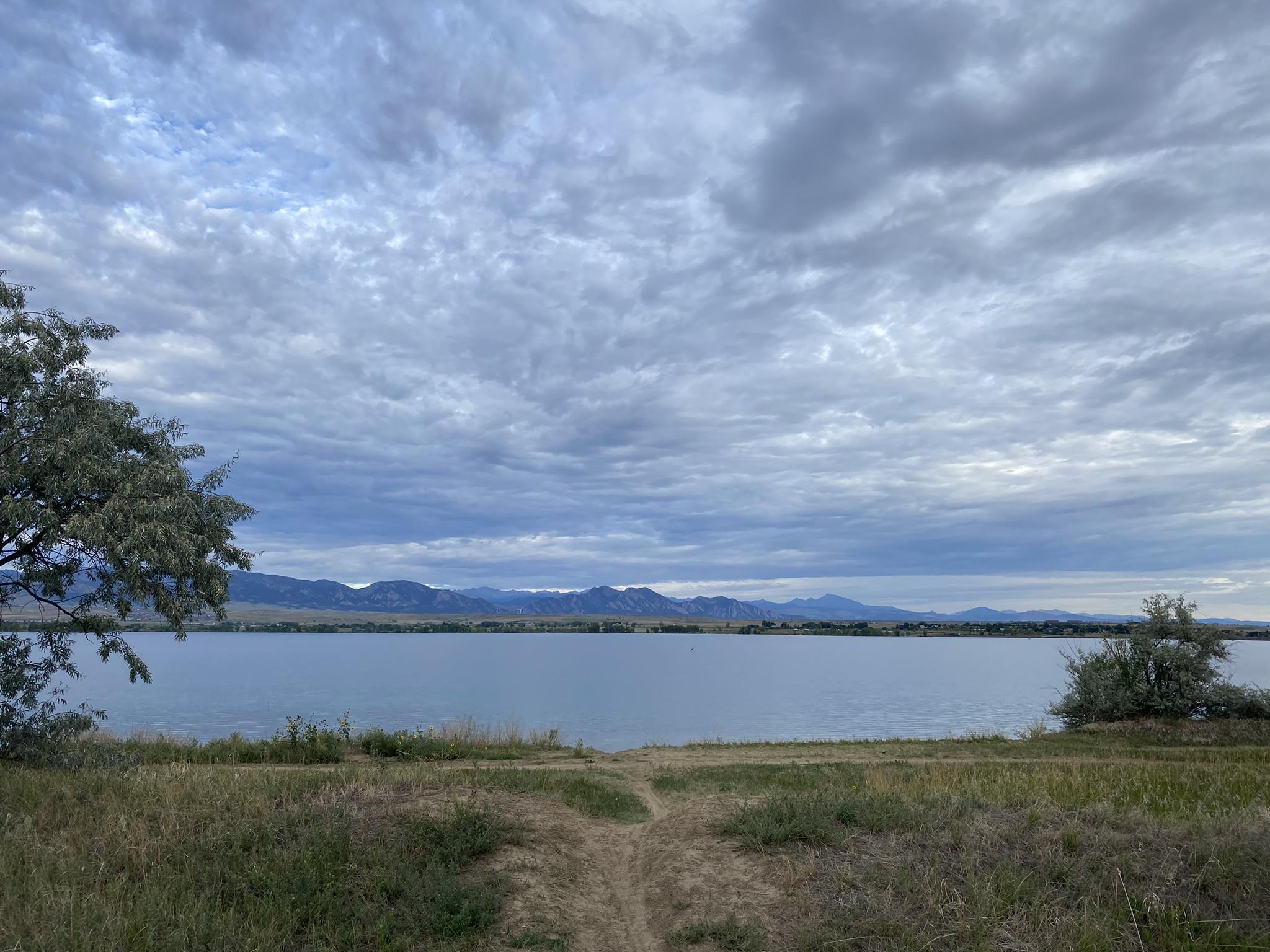 A calm lake with distant mountains under a cloudy, overcast sky.