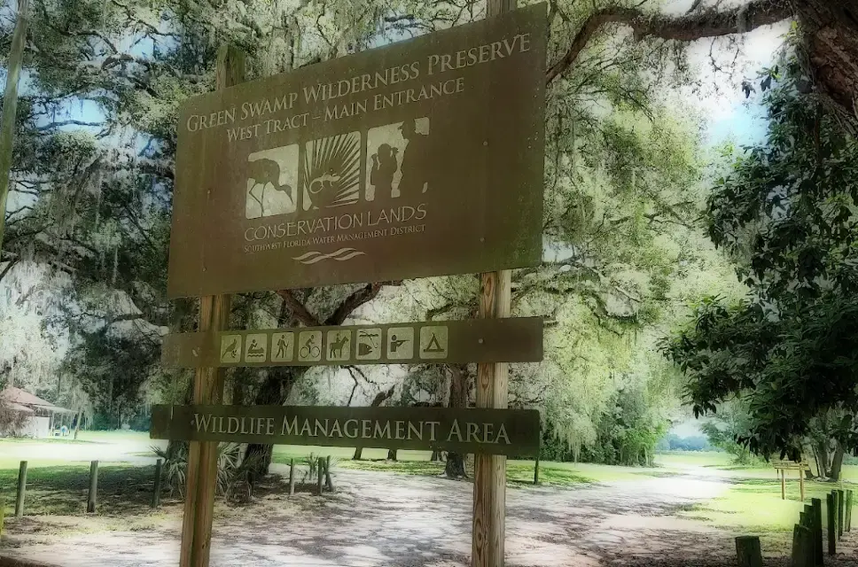 Large wooden sign for a wilderness preserve, surrounded by mossy trees.