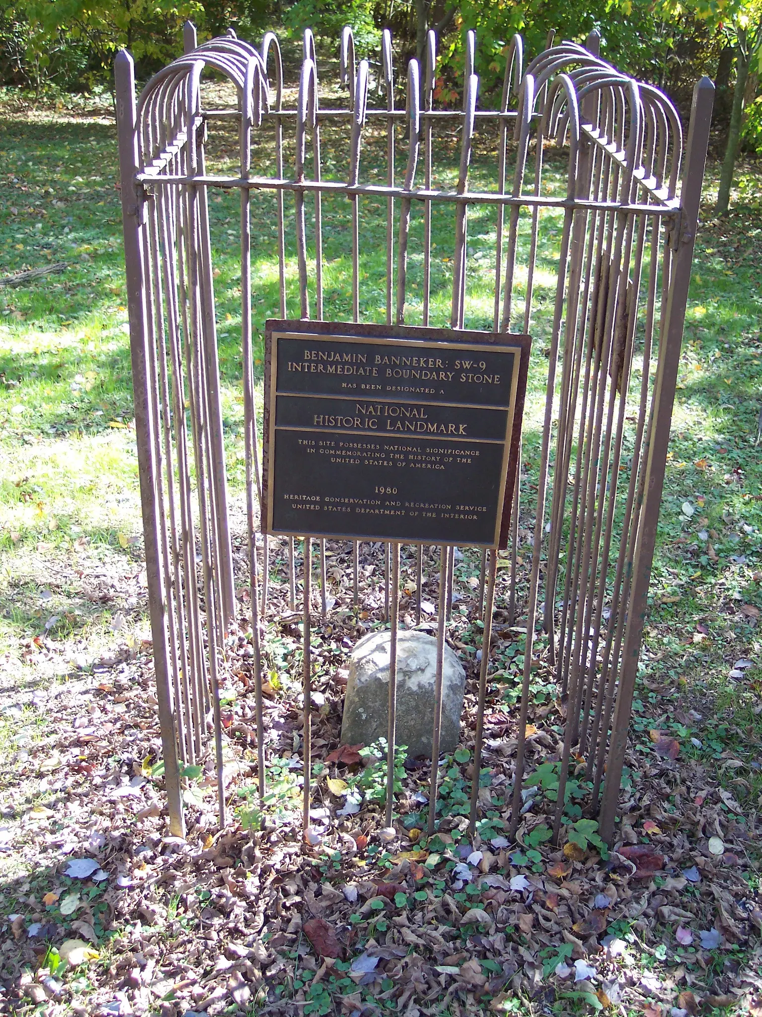 A historical plaque on a stone, protected by a metal cage in nature.