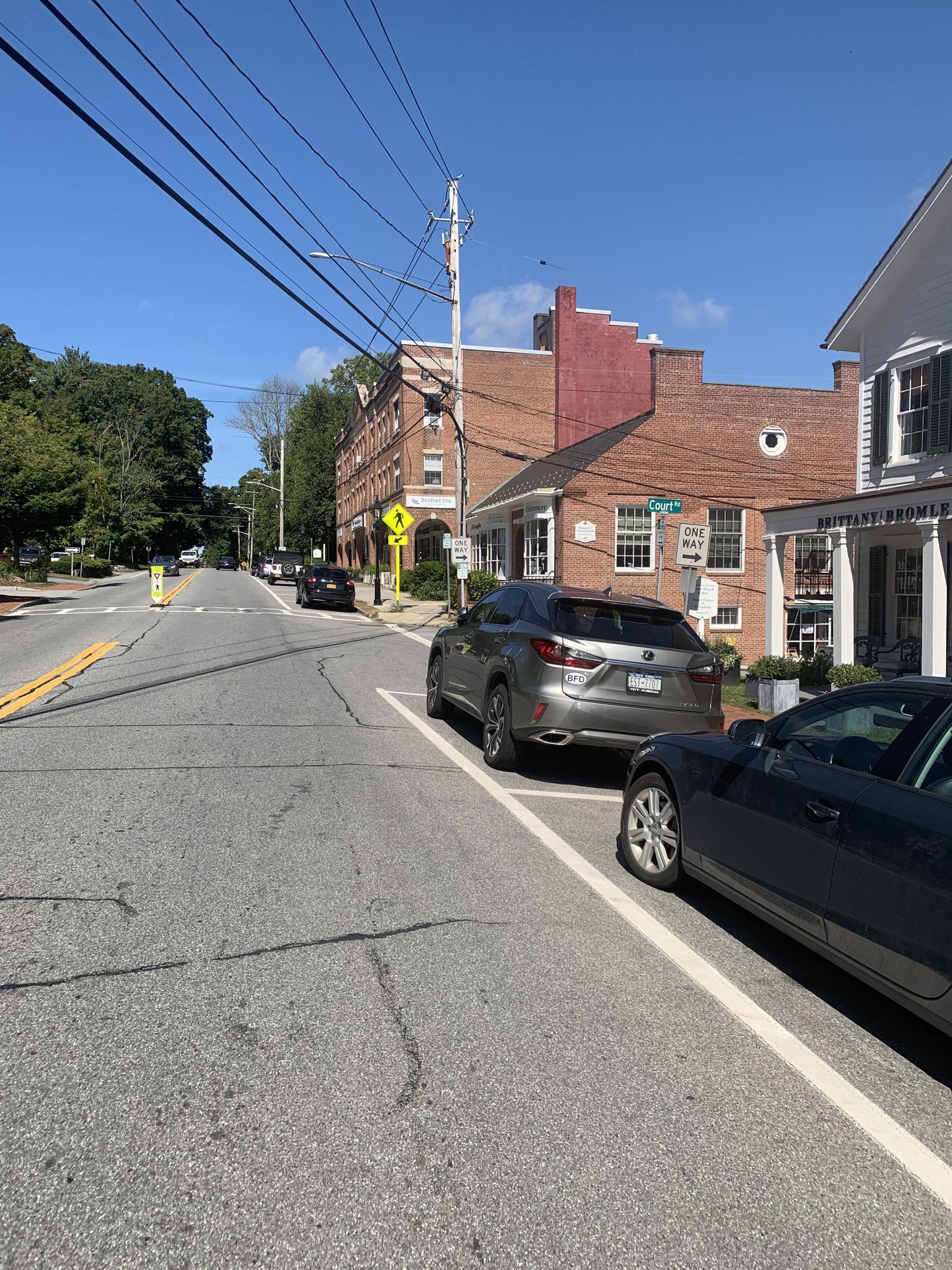 Sunny street scene with parked cars and brick buildings.