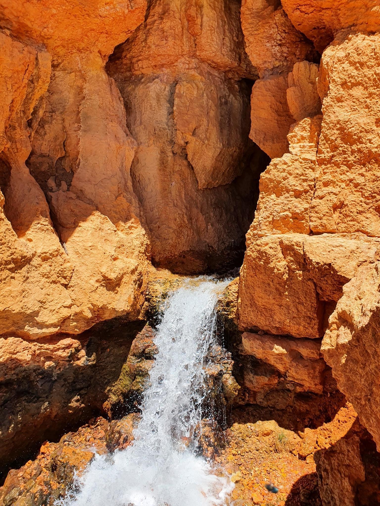 Waterfall cascading down orange rock formations into a sunlit pool.