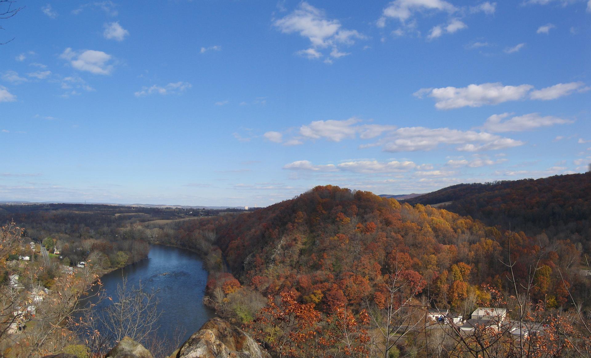 Scenic autumn landscape with a winding river, colorful hills, and blue sky.
